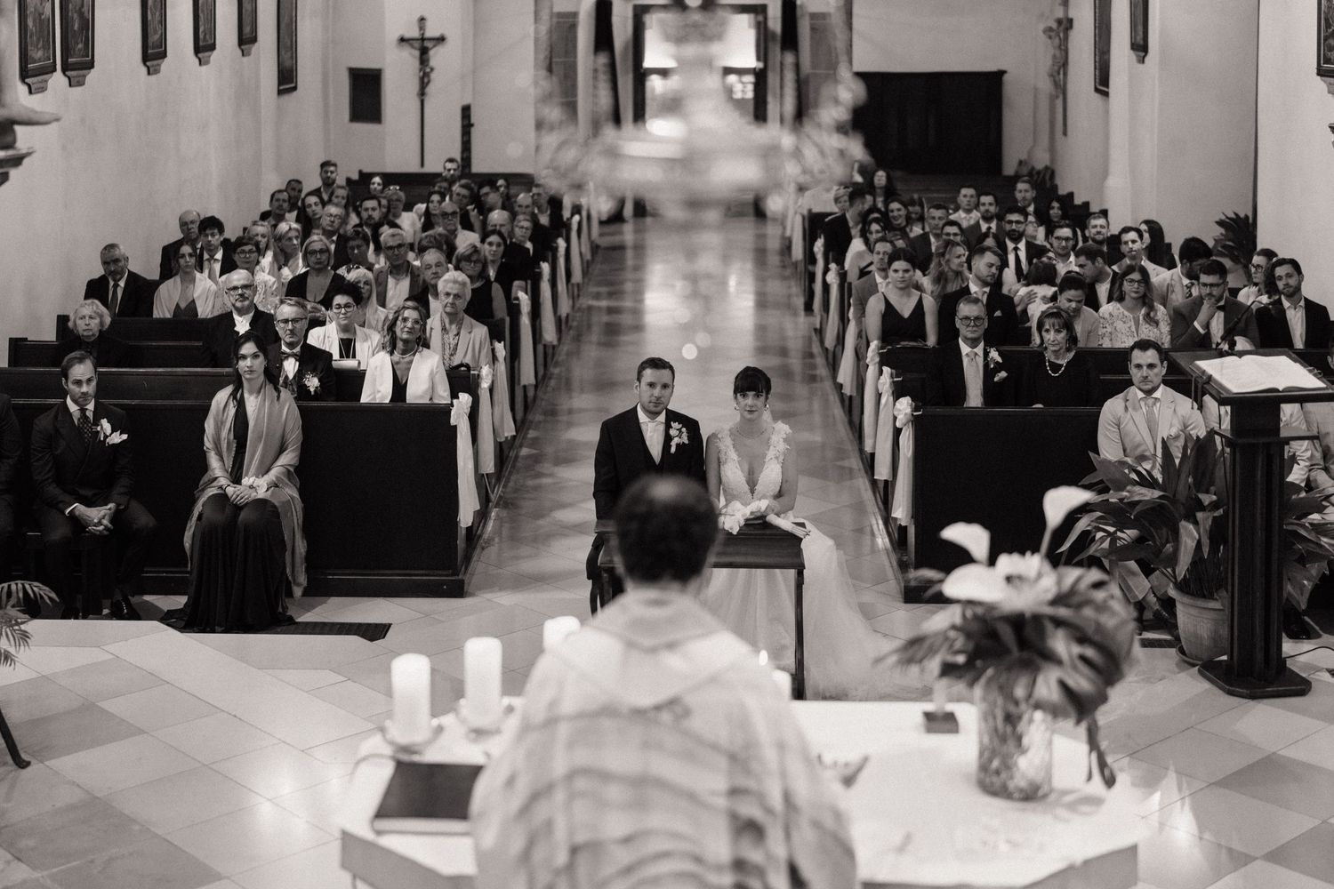 Black and white wedding ceremony photo inside a church with guests seated in pews as couple stands at the altar.