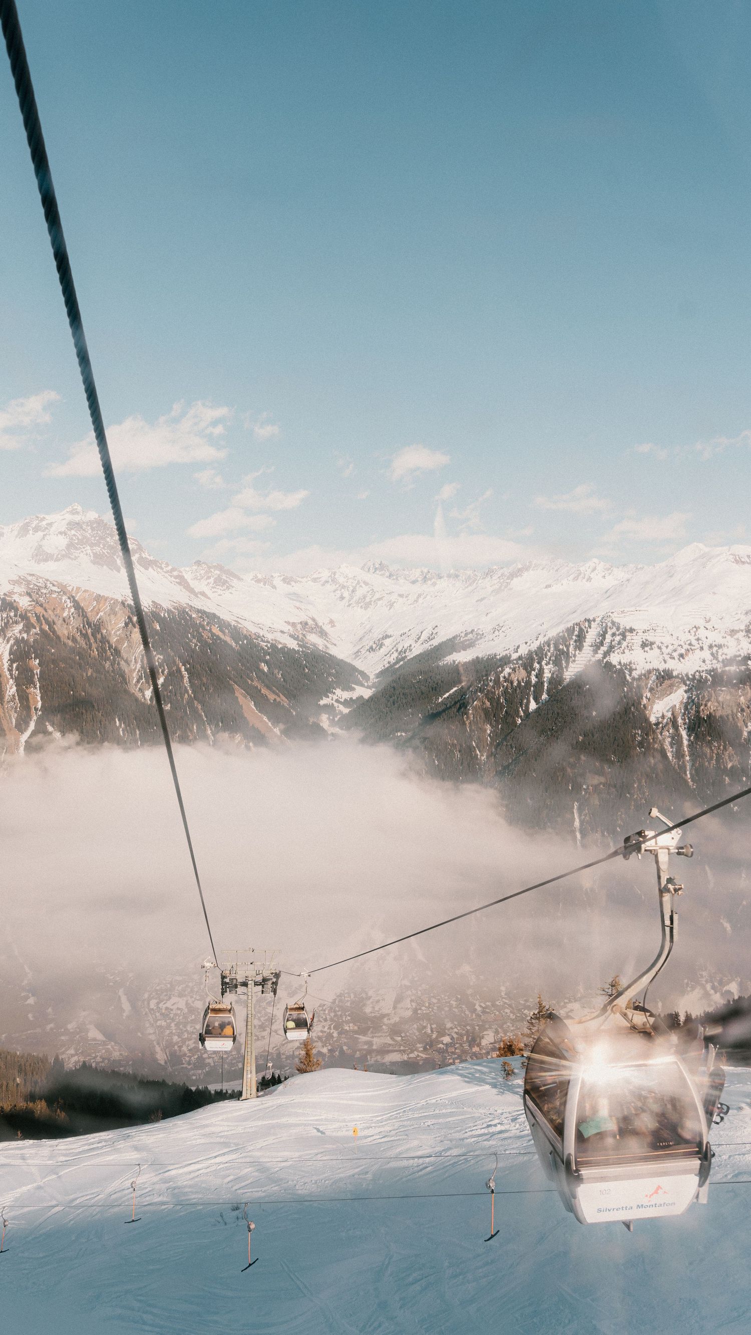 Ski lift chairs ascending through misty mountain landscape with snow-capped peaks.