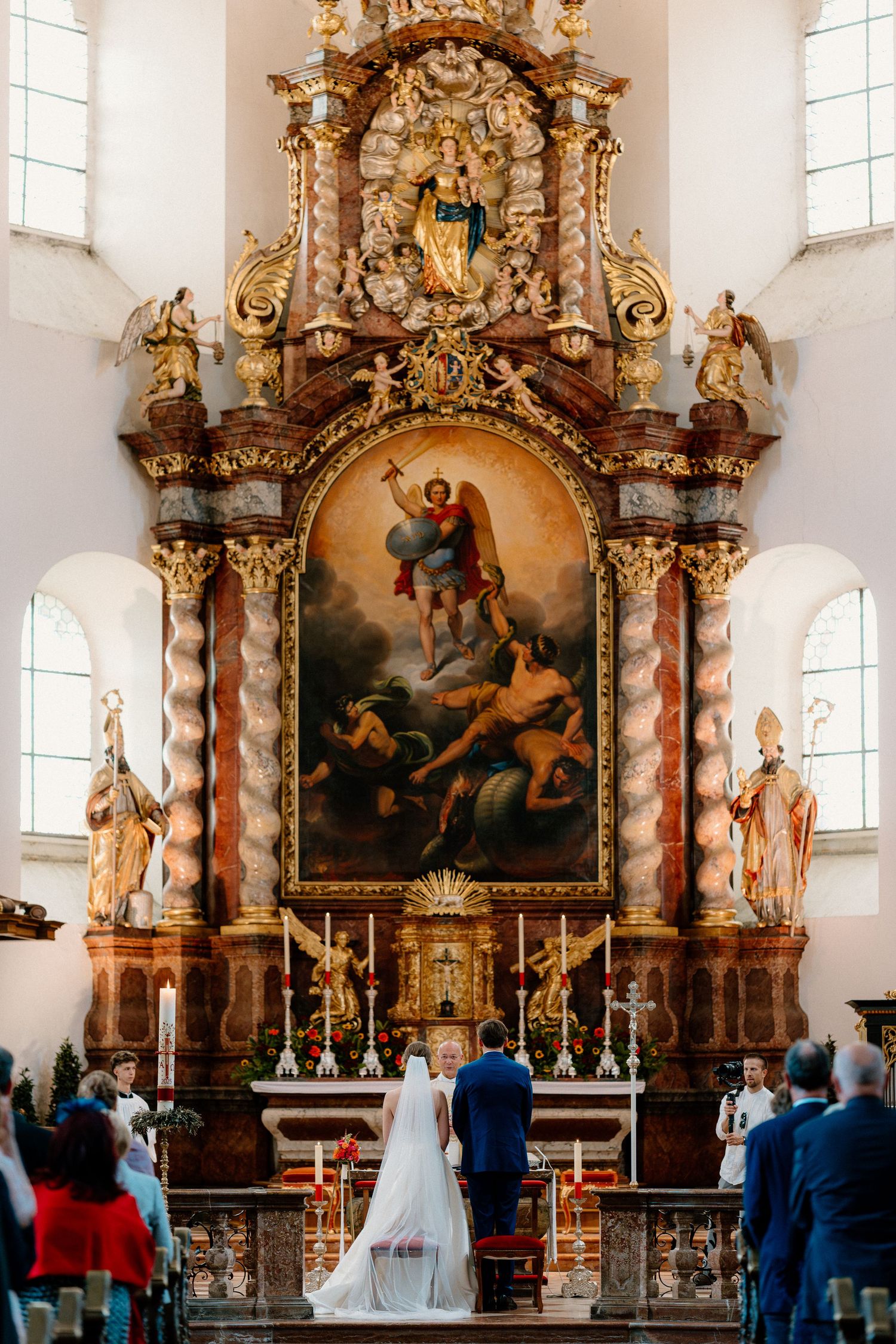 Baroque church altar with gilded decorations and religious paintings during a wedding ceremony.