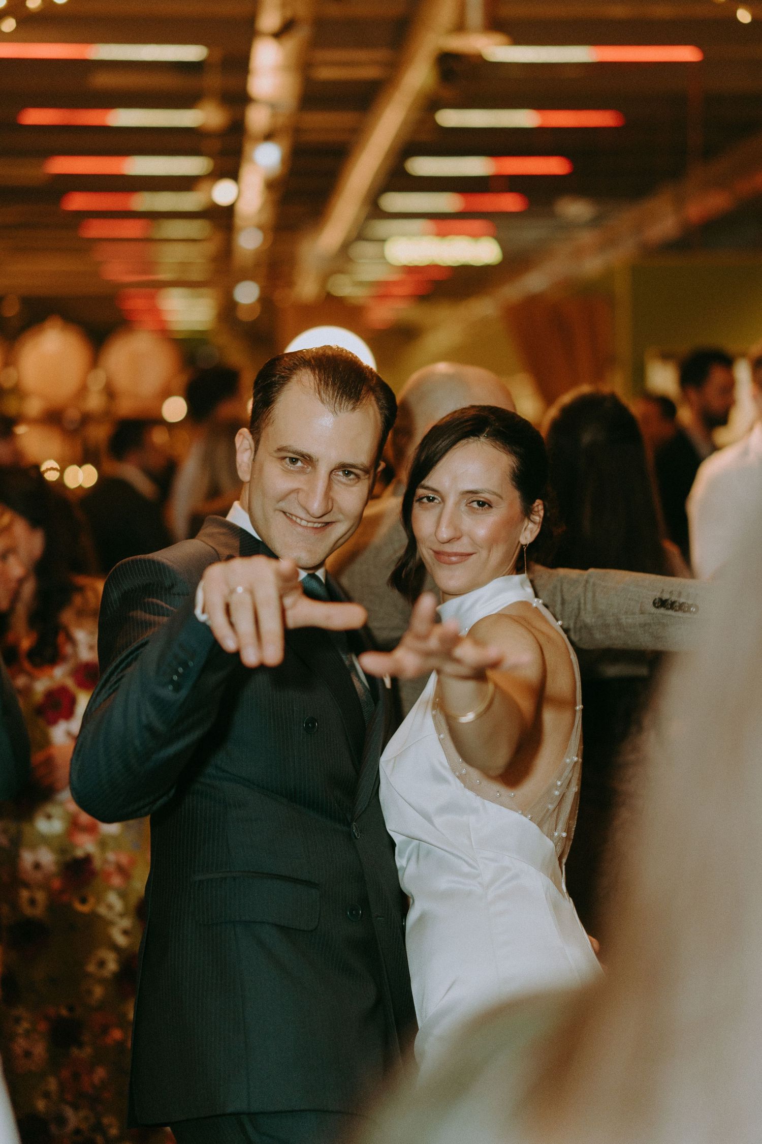 Wedding celebration with guests dancing and enjoying festivities in dimly lit venue.