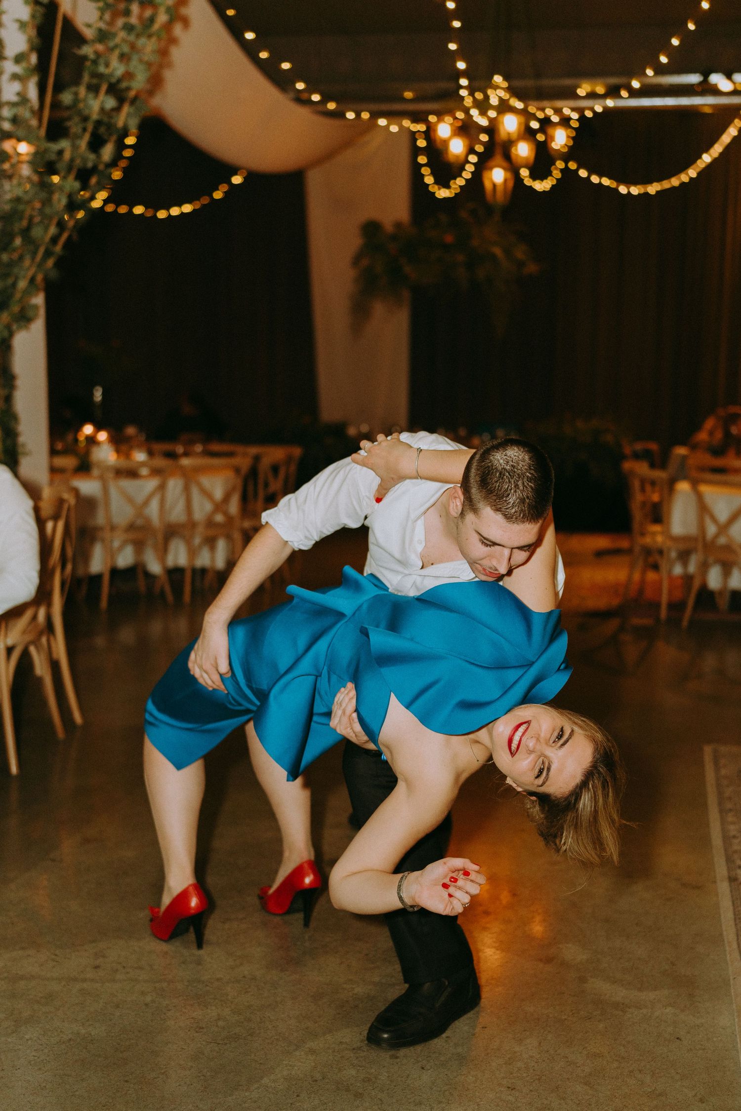 Wedding guests perform a fun dance routine on the reception floor with string lights glowing overhead.