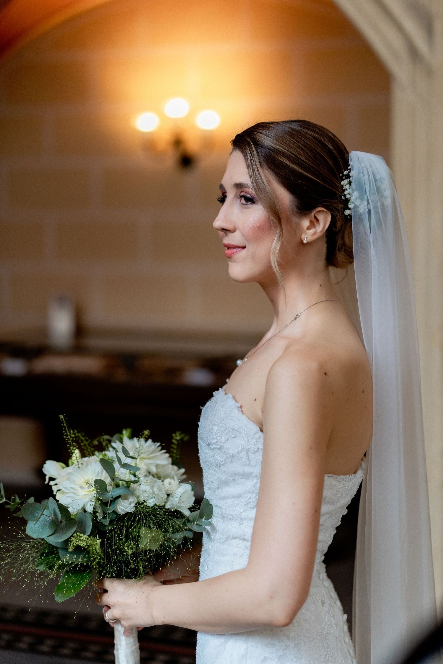 A bride holds a white and green bouquet while posing in an elegant indoor setting.