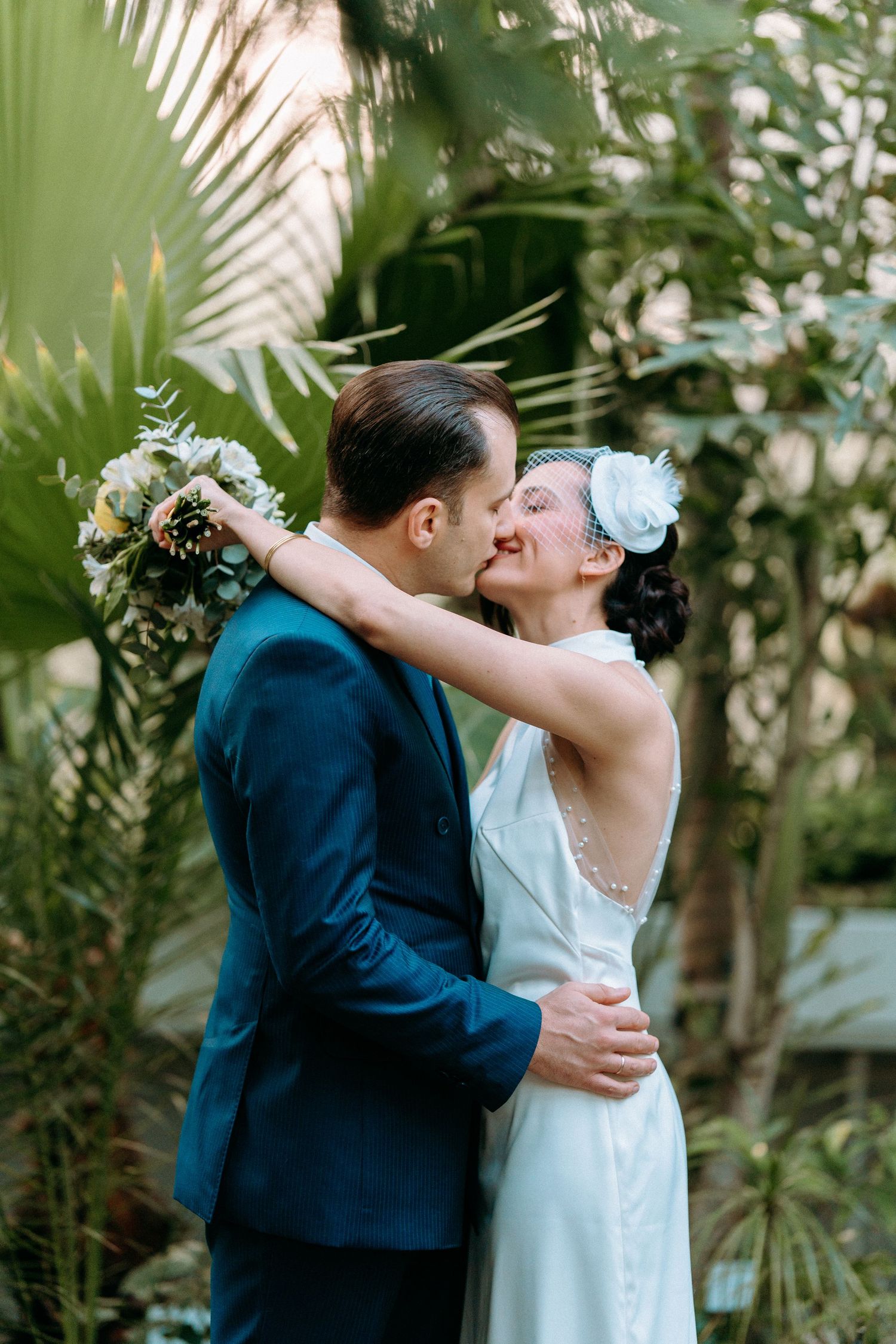 Romantic wedding couple sharing a kiss in a lush tropical garden setting with palm fronds.