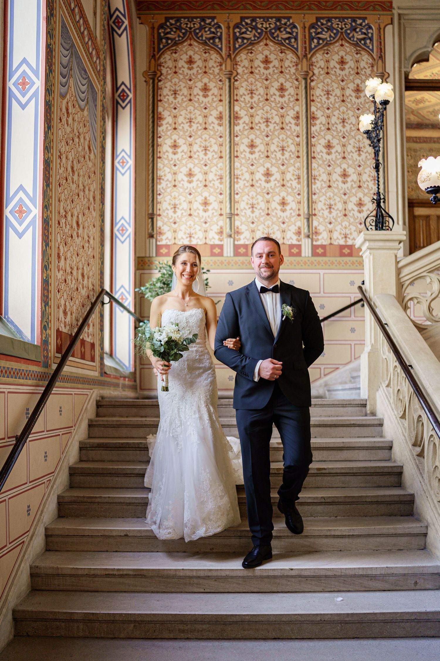 Wedding processional along an ornate Victorian staircase with floral wallpaper.
