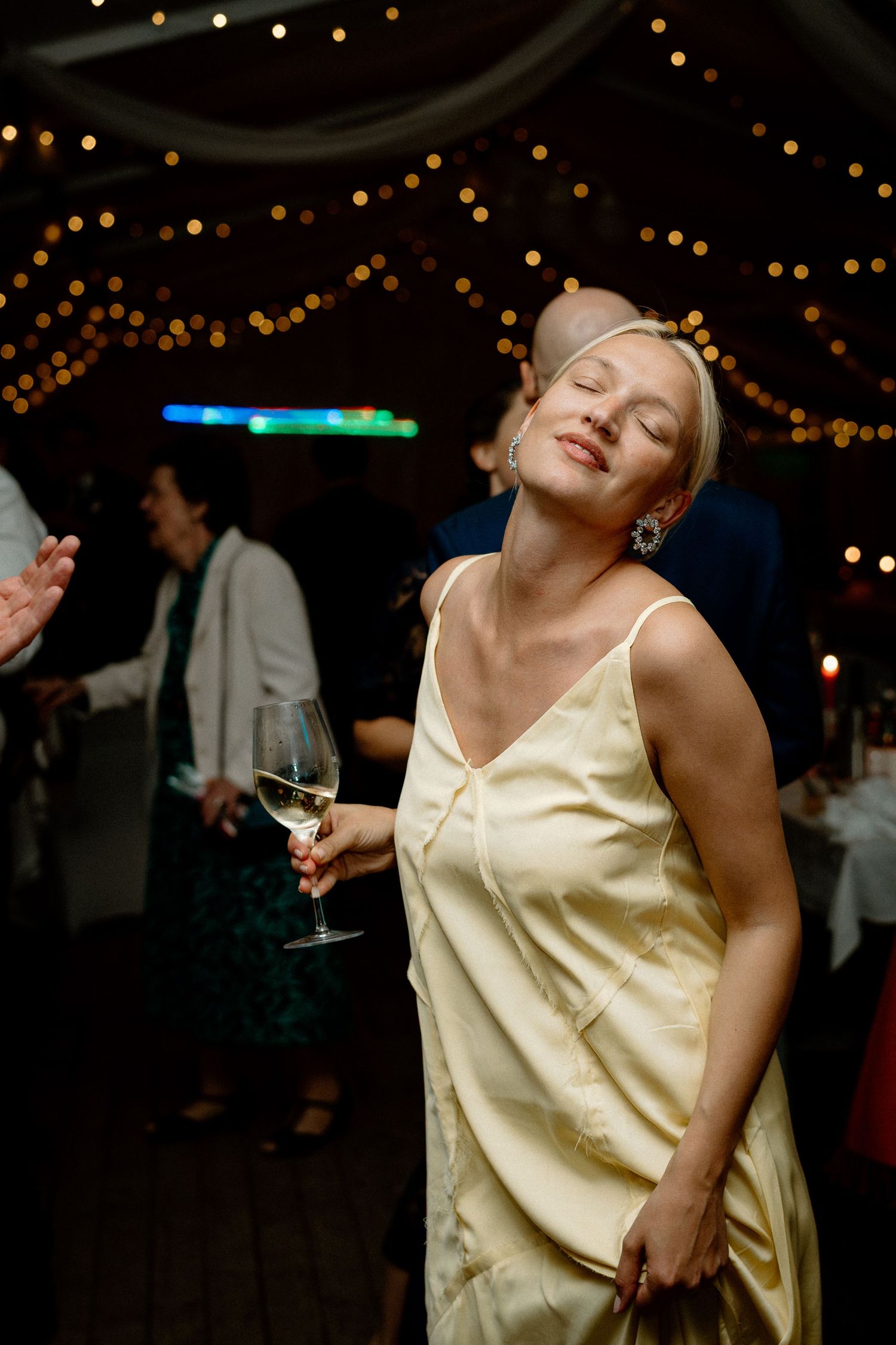 A guest in a cream dress dancing at a wedding reception under twinkling lights.