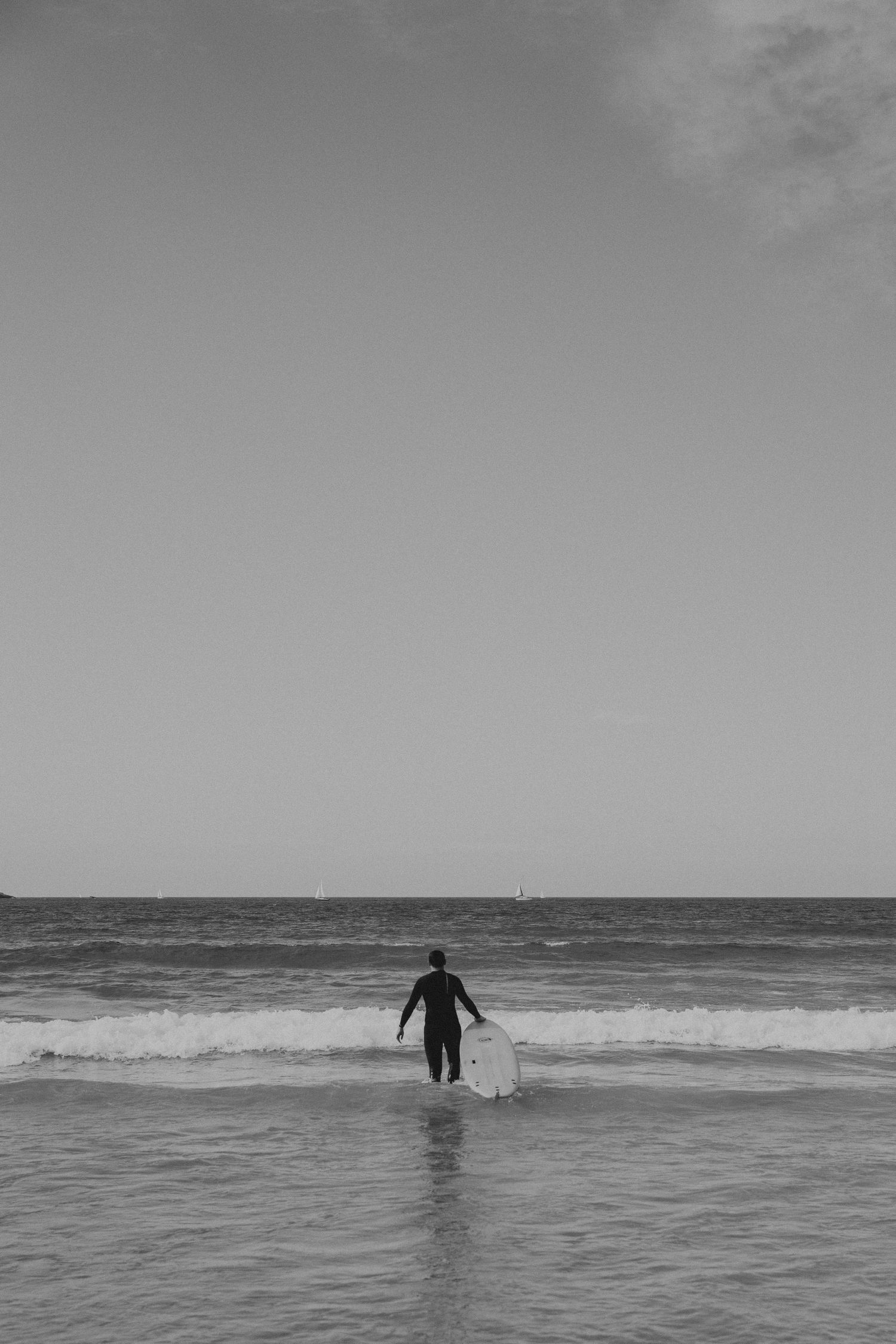 A lone surfer wades into choppy ocean waves under an overcast sky.