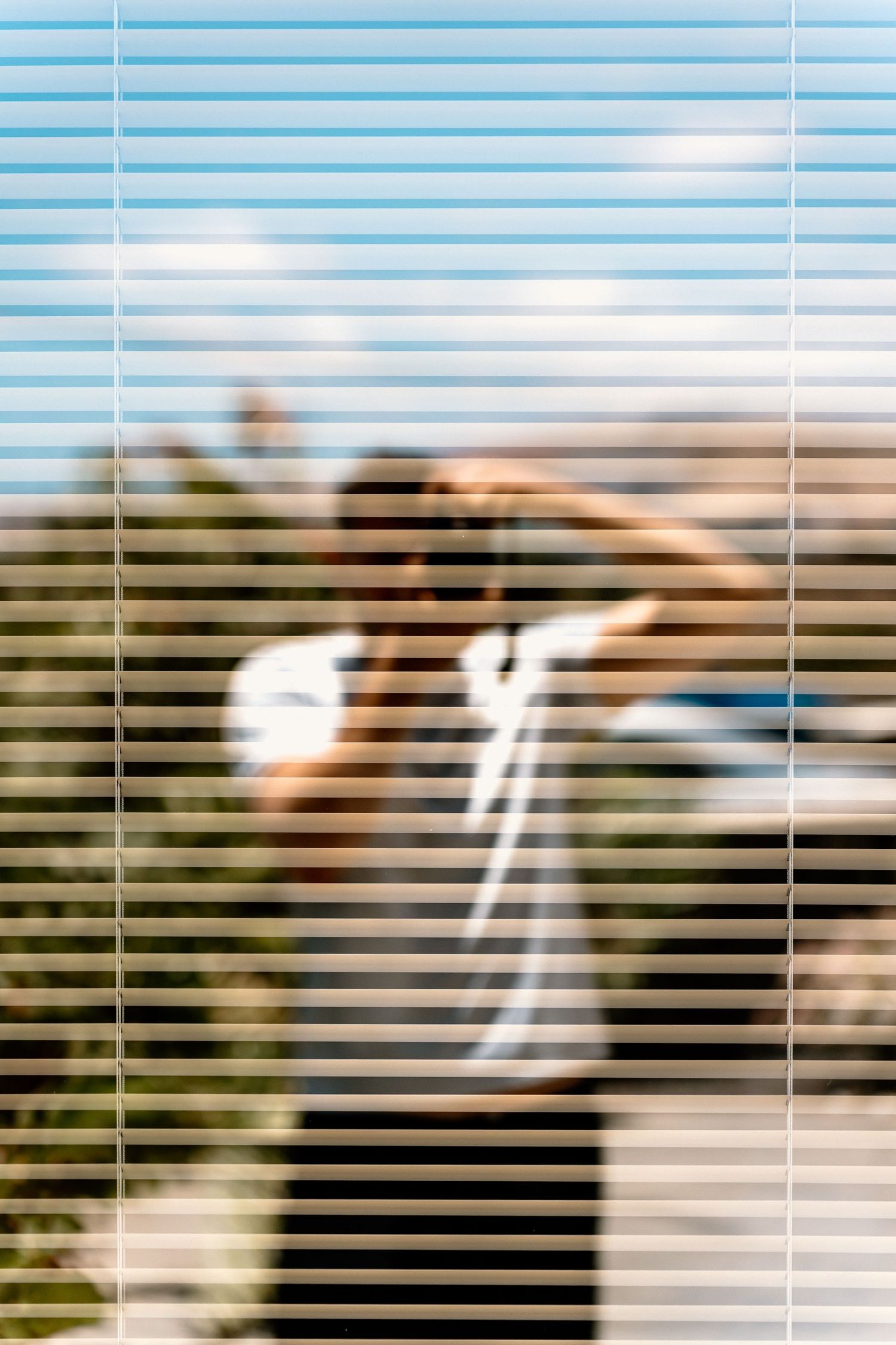 A series of horizontal window blinds creating a striped pattern effect against a blurred background.