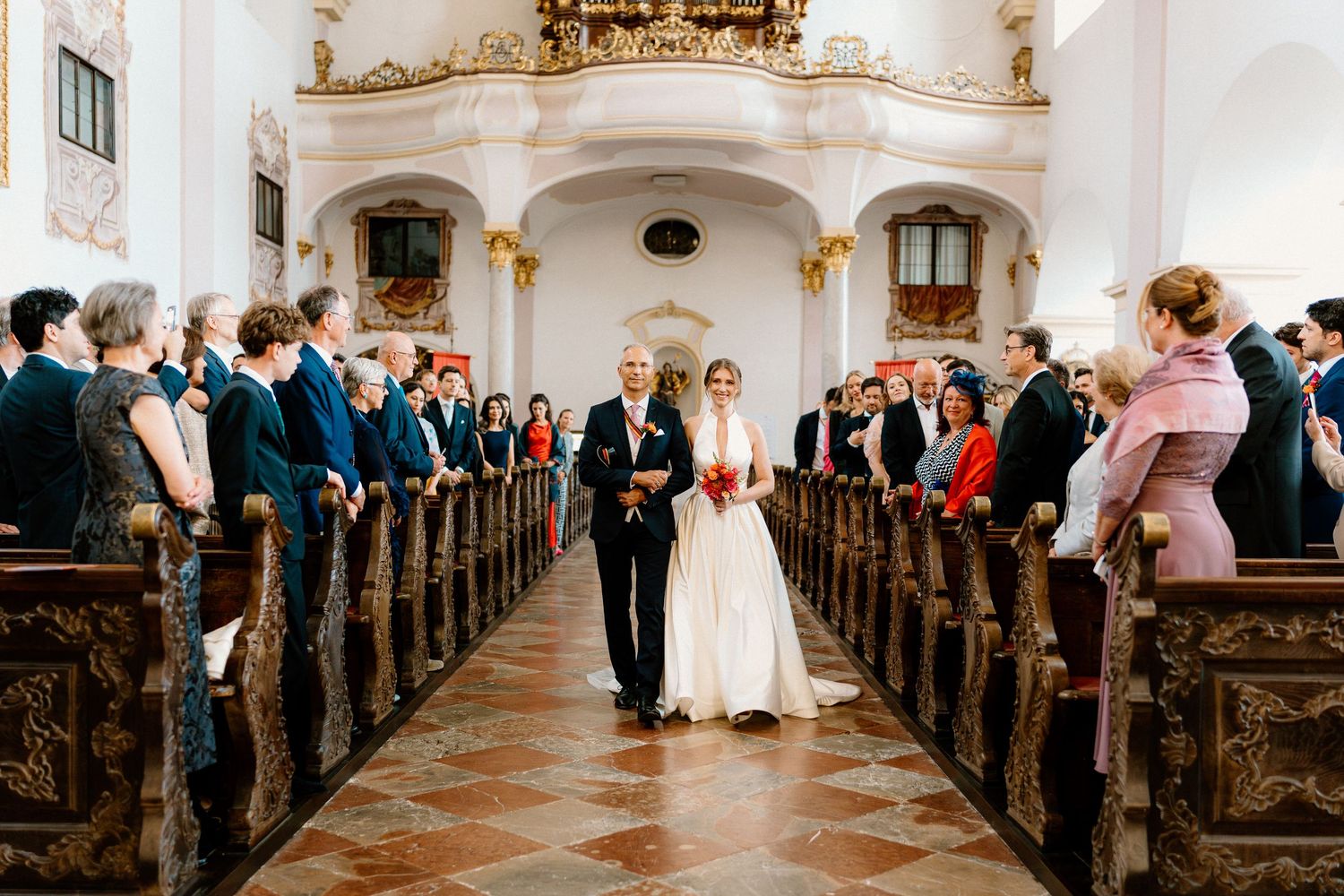 Elegant church interior with ornate wooden pews and guests gathered for a wedding ceremony.