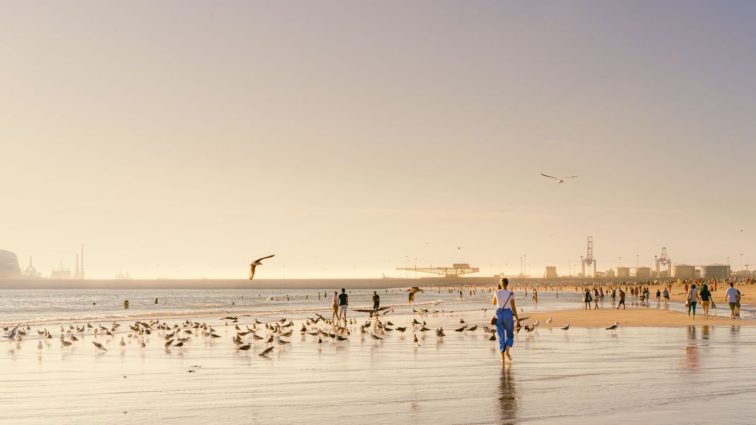 Wide sandy beach with scattered people walking along the shoreline on a misty day.