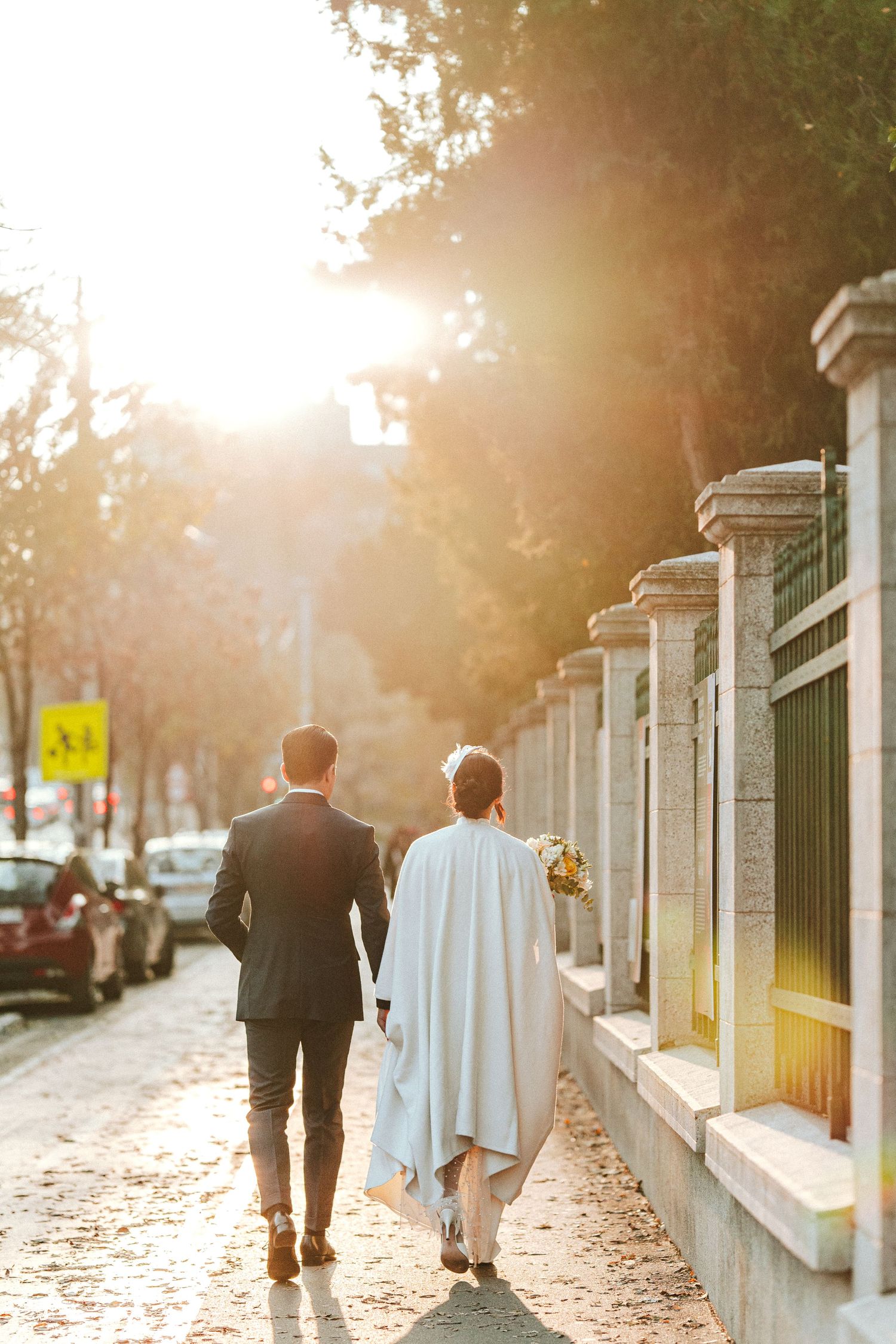 Two people walk together on a sunlit path along a white wall during golden hour.