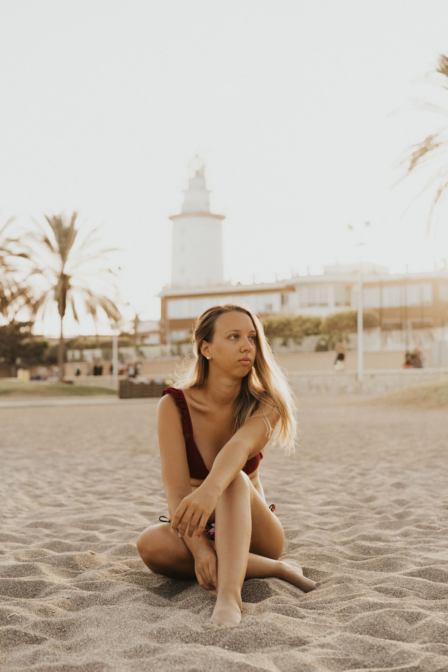 Person lounging on sandy beach at sunset with palm trees in background.
