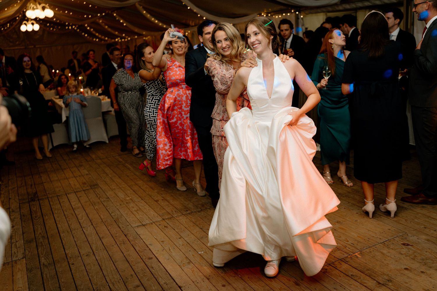 Wedding reception dancers enjoying themselves on a wooden dance floor under string lights.