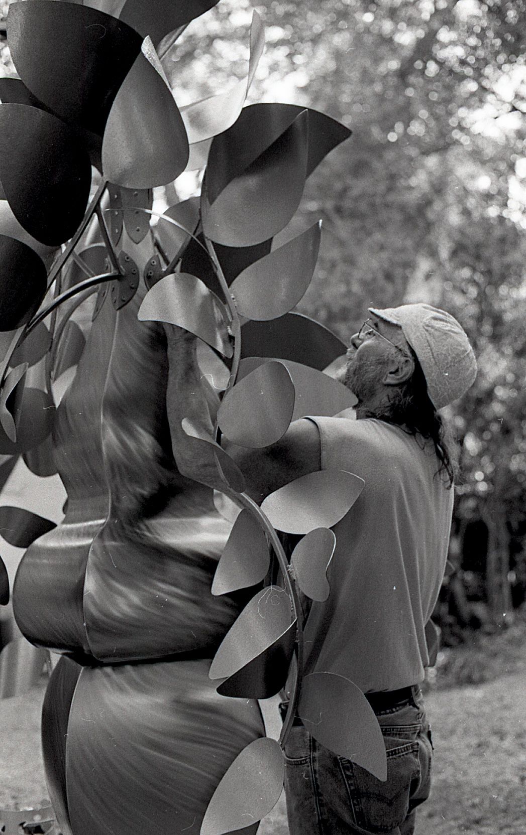 Black and white close-up of a person examining a large decorative metal leaf sculpture outdoors.