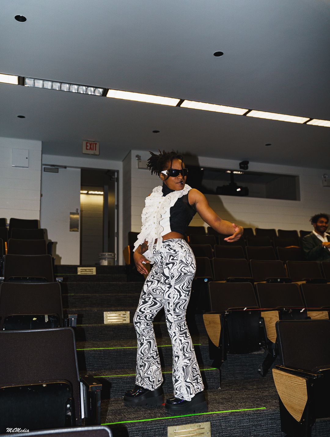 Model in black-and-white swirl flared pants and ruffled top poses in auditorium aisle.
