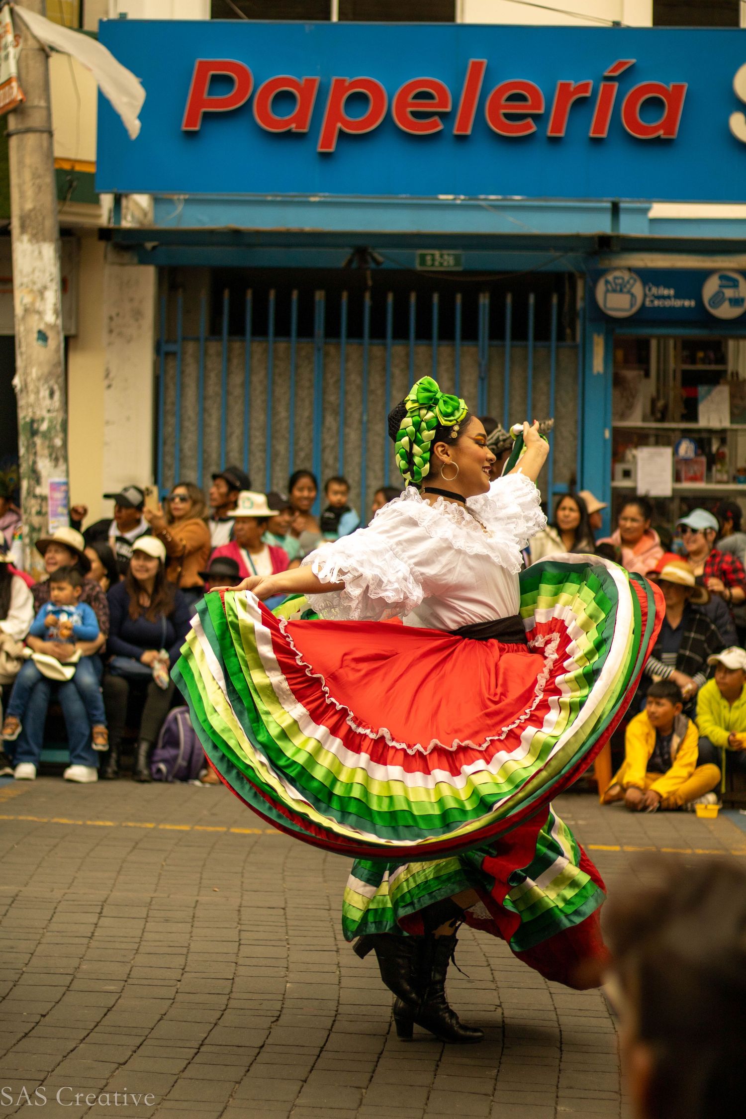 Female dancer twirling a vibrant red and green folkloric dress outside a Papeleria store.