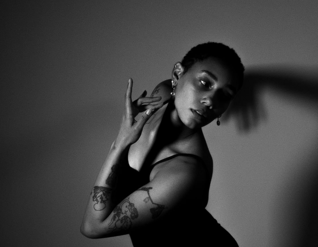 Dramatic black and white portrait of a tattooed woman posing gracefully against a shadowed studio background.