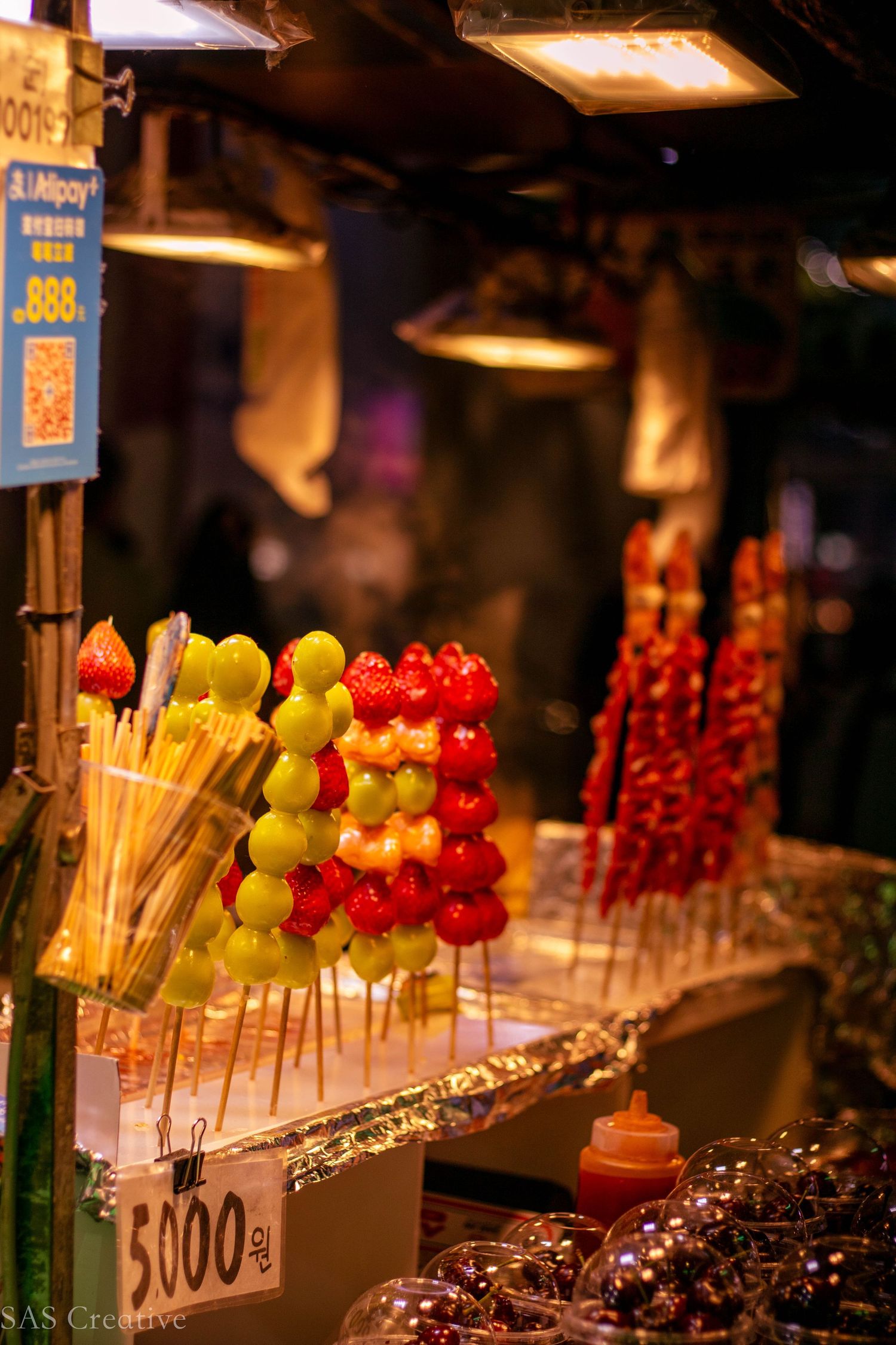 Colorful fruit skewers with grapes and strawberries at a night market food stall.