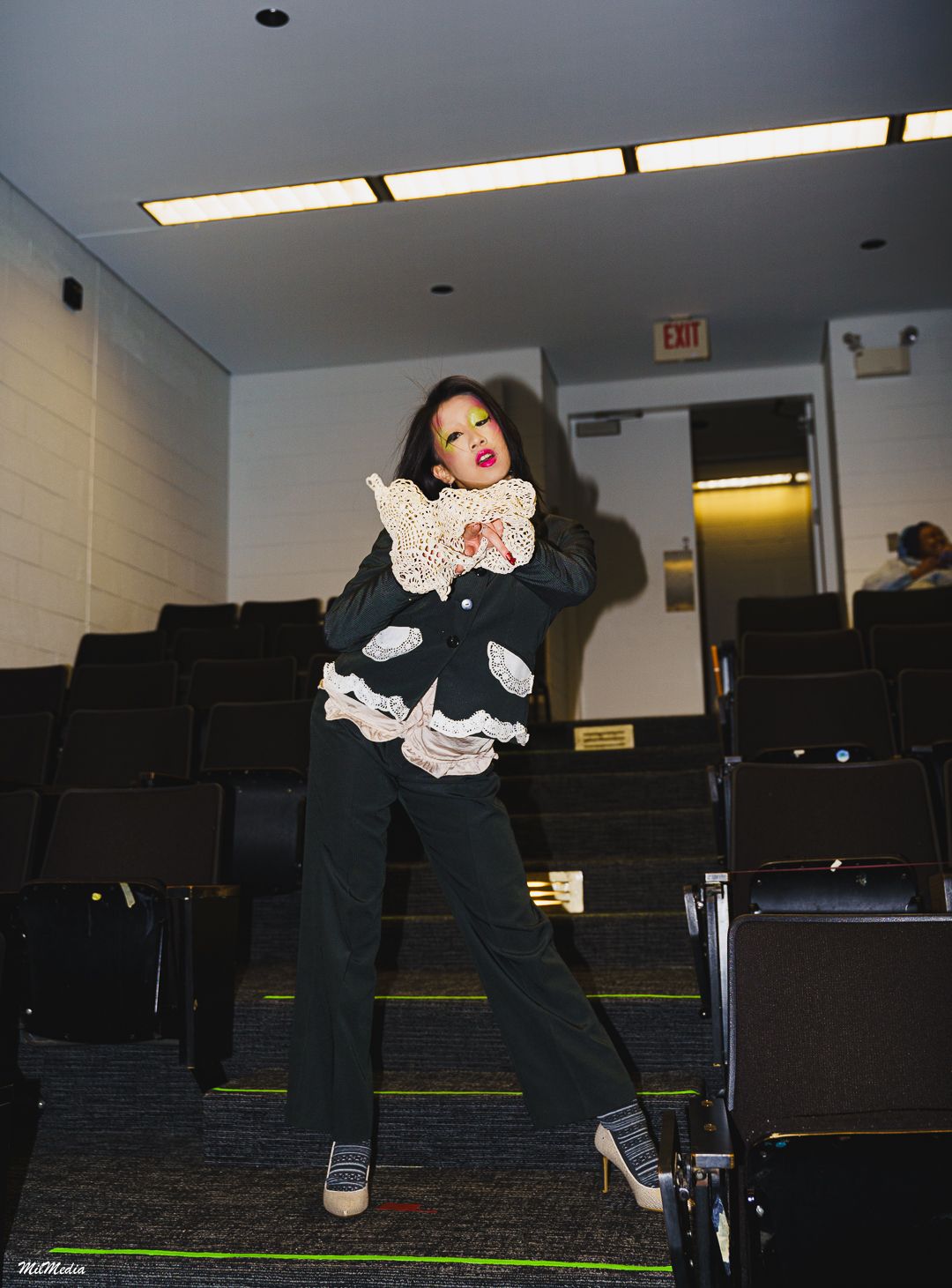 A performer in black pants and a ruffled top strikes a pose in an empty auditorium.