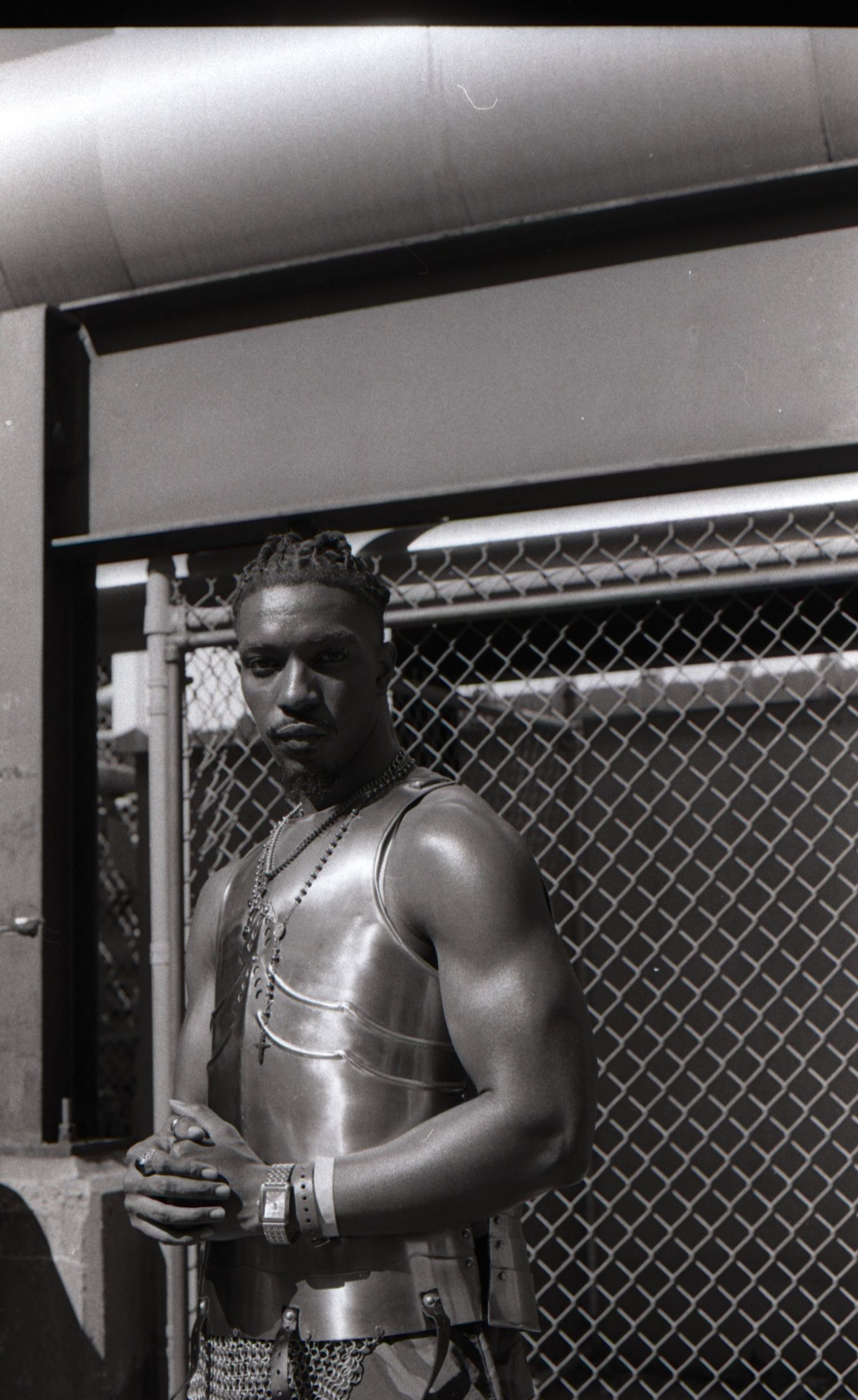 Black and white photo of a man in a shiny vest holding a staff beside a chain-link fence.