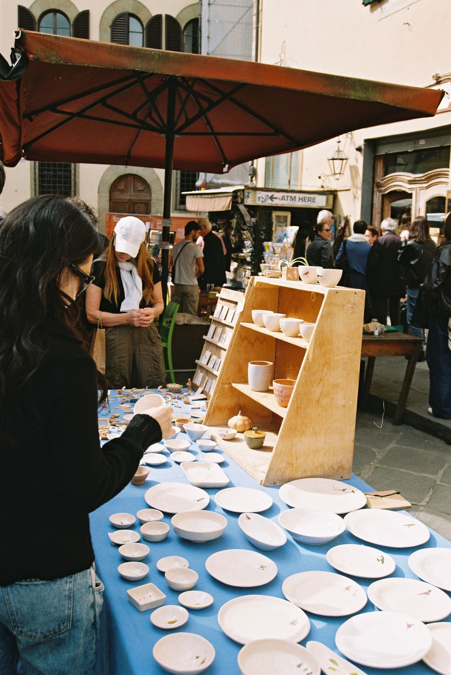Woman browsing white ceramic plates and bowls at an outdoor market stall in Florence, Italy.