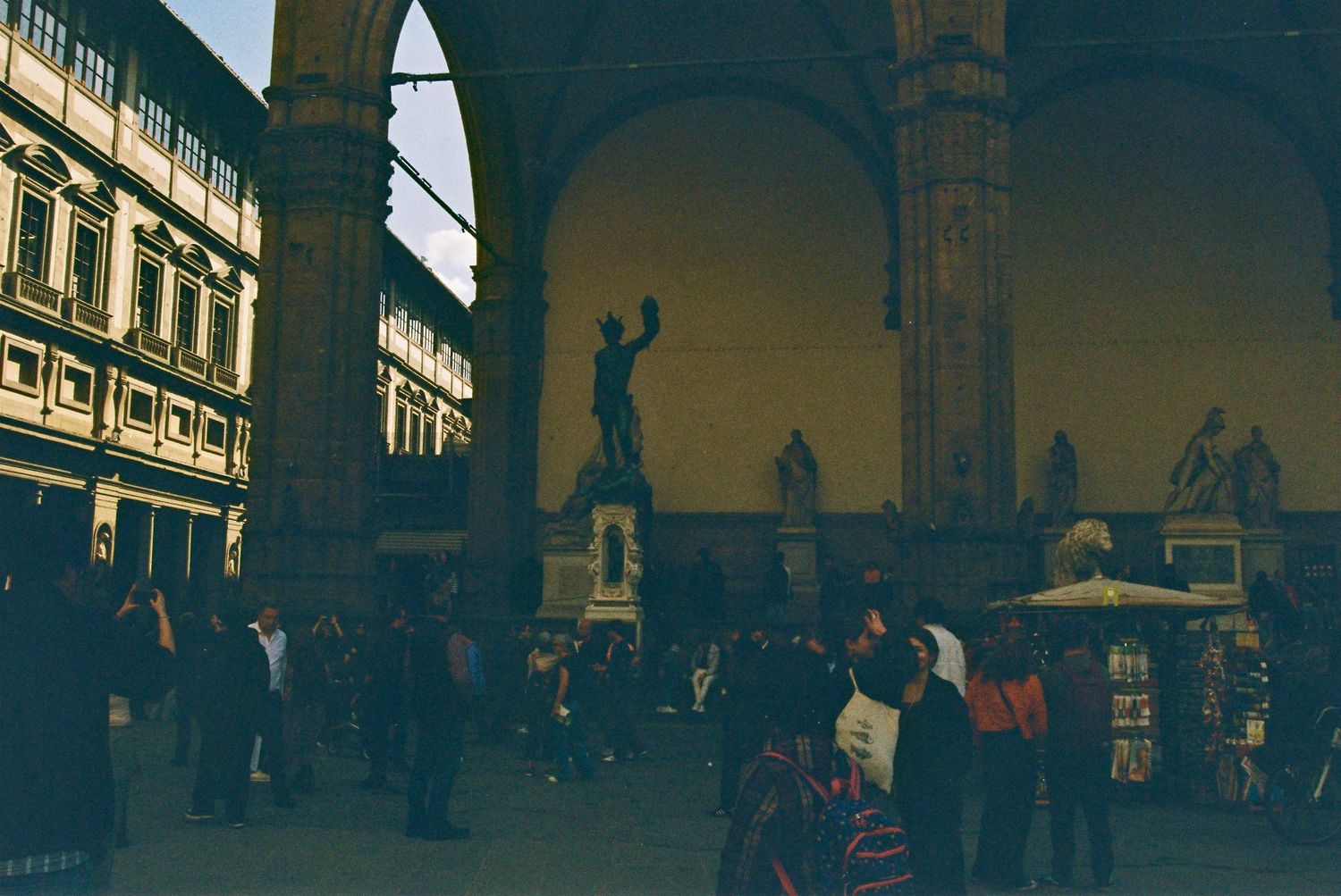 Tourists explore the Piazza della Signoria in Florence with classical sculptures and the Uffizi Gallery.