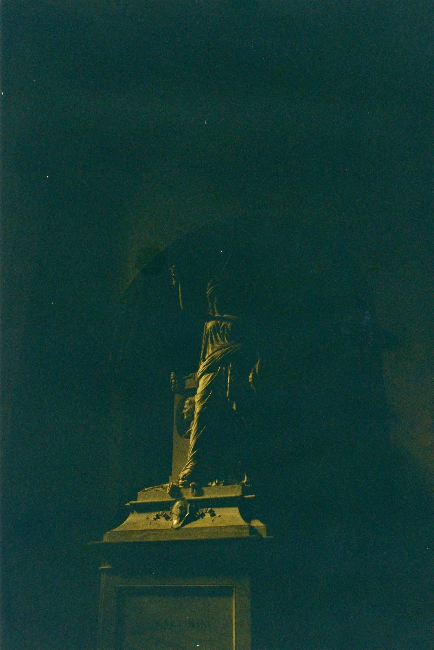 Dark moody photograph of a classical statue on a pedestal illuminated in golden light.