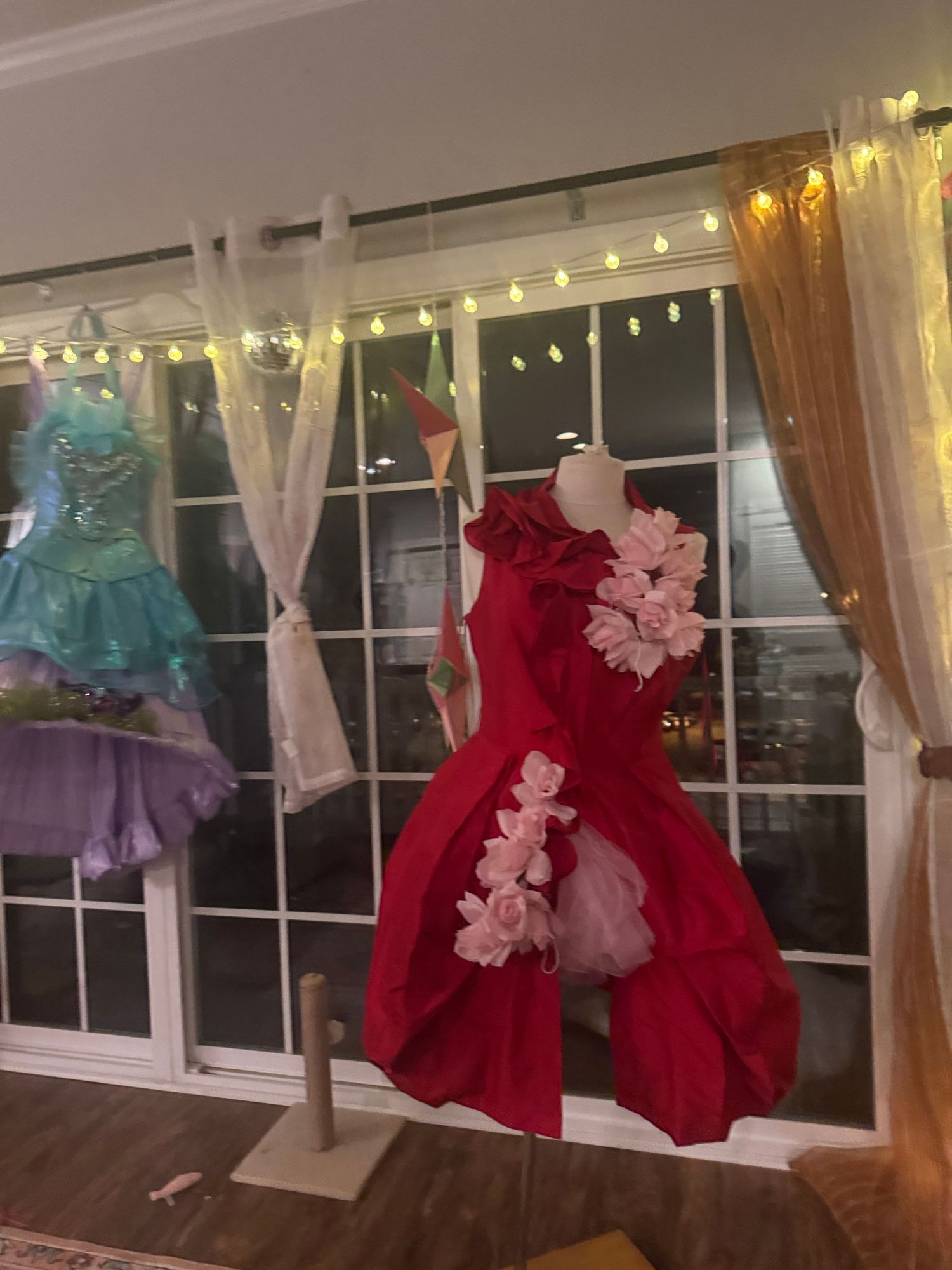 Red floral dress displayed on a mannequin near a window with fairy lights and curtains.