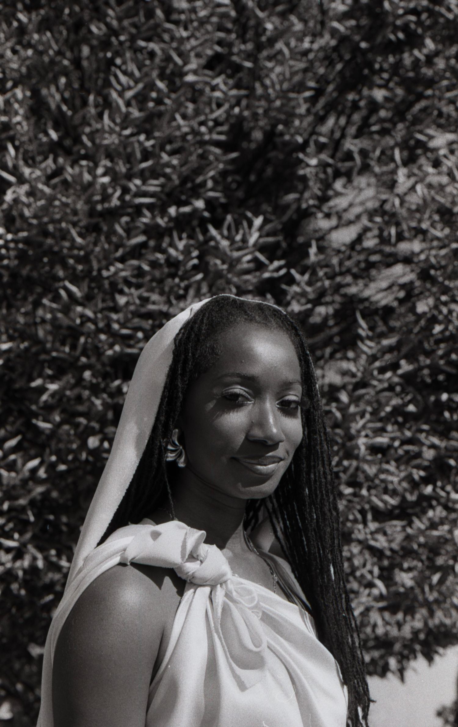 Black and white portrait of a young Black woman with braids wearing a white draped dress outdoors.