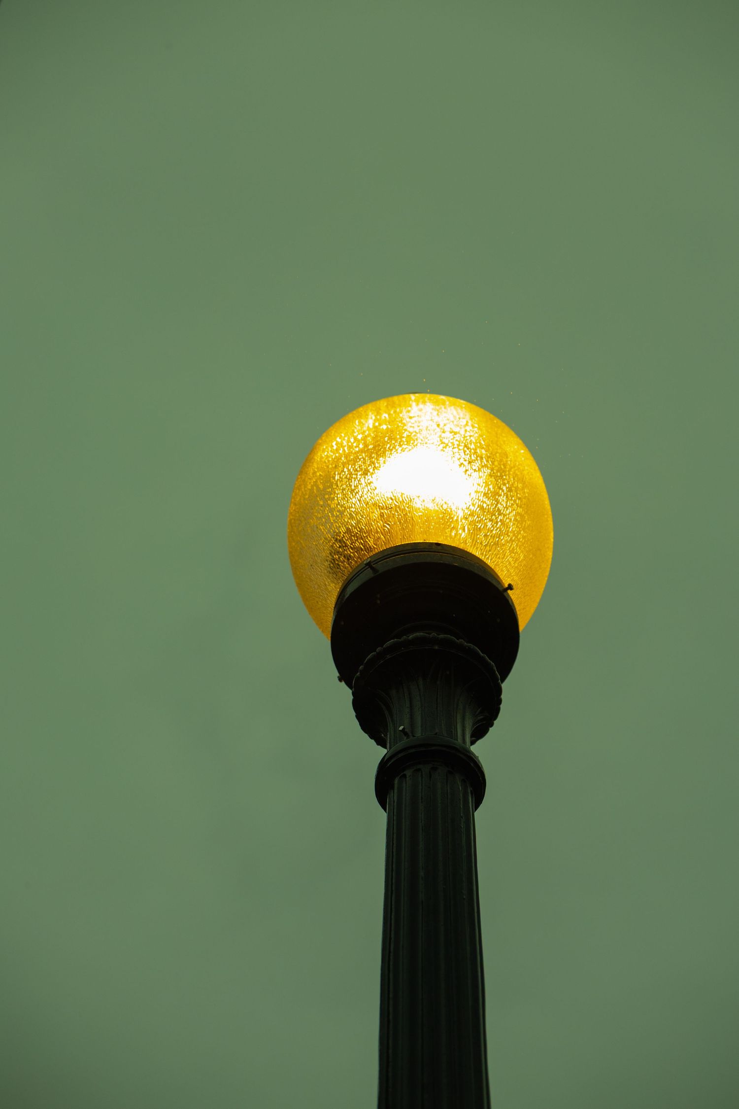 Glowing golden globe street lamp against a muted green sky at dusk.