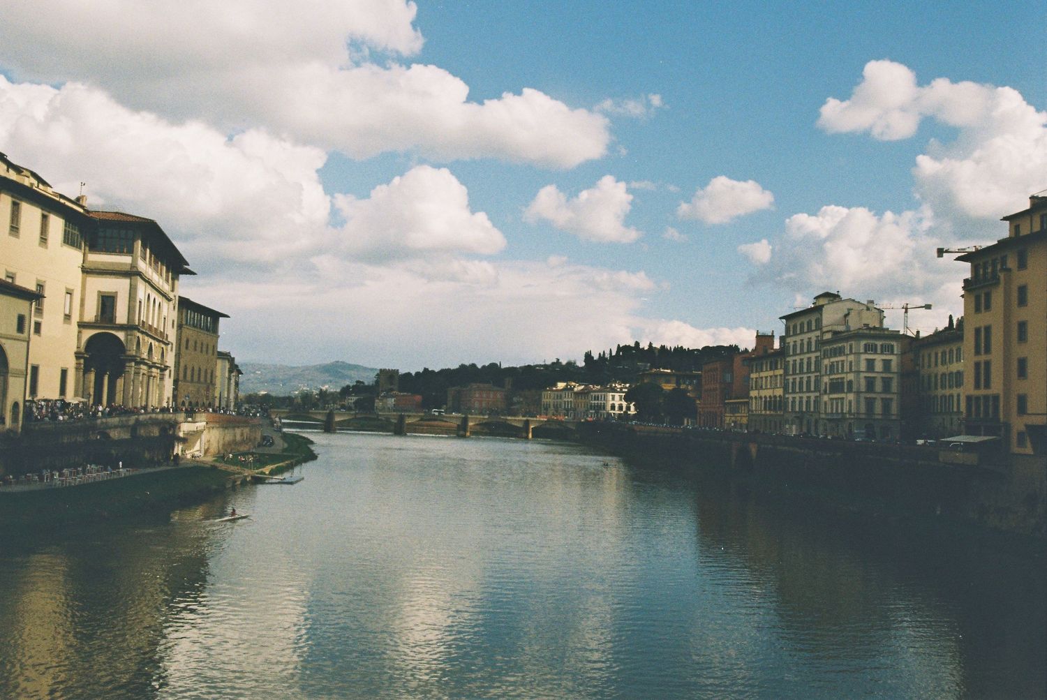 Panoramic view of the Arno River in Florence, Italy, with historic buildings and dramatic cloudy sky.