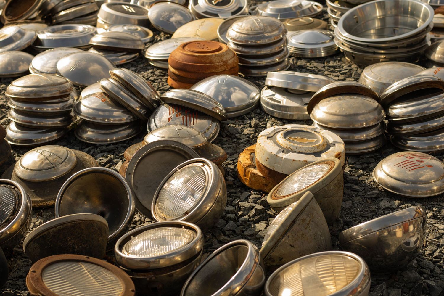 Large collection of vintage car hubcaps and headlights scattered on ground.