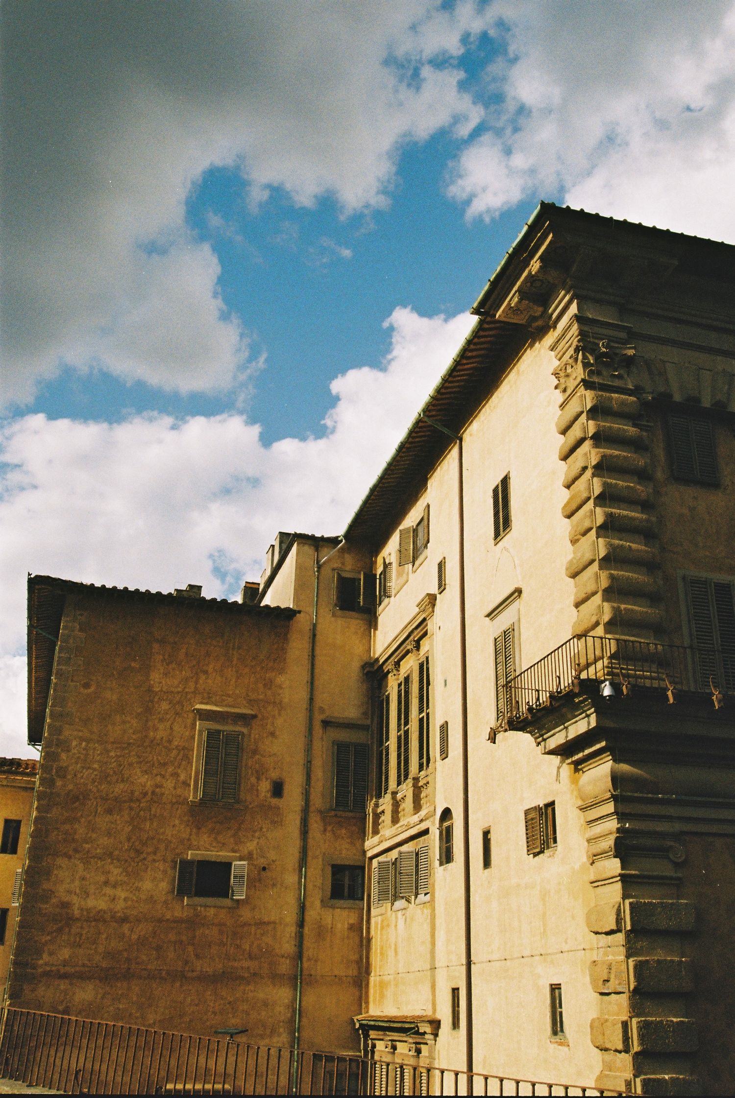 Low-angle view of historic Italian Renaissance buildings with ornate stonework against a bright blue cloudy sky.