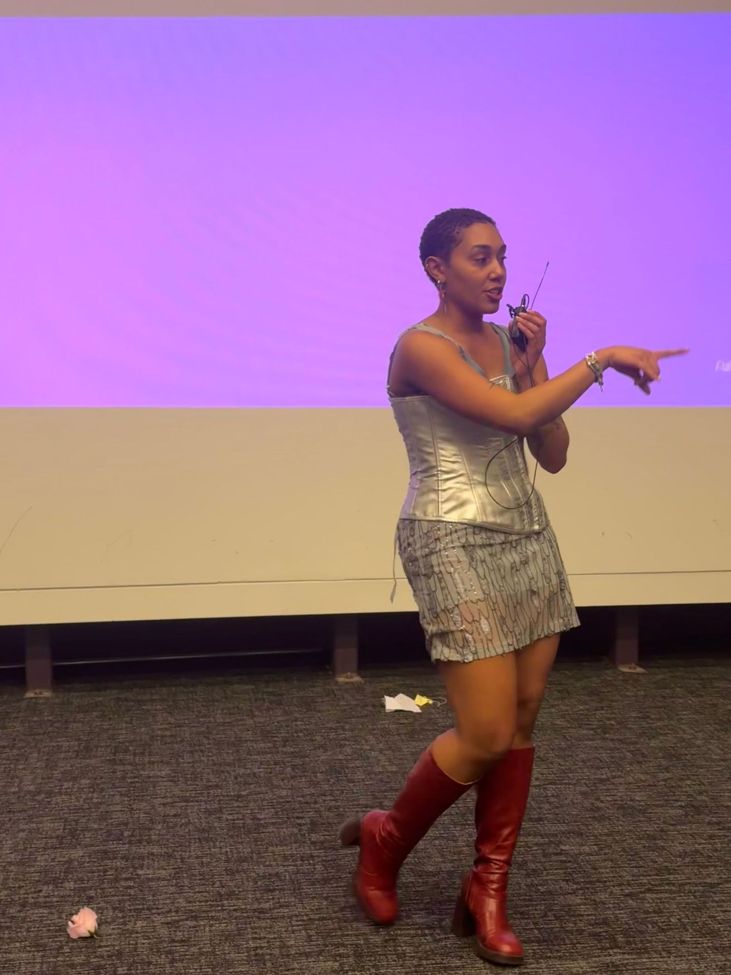Woman in silver metallic mini dress and red boots performing on stage with microphone.