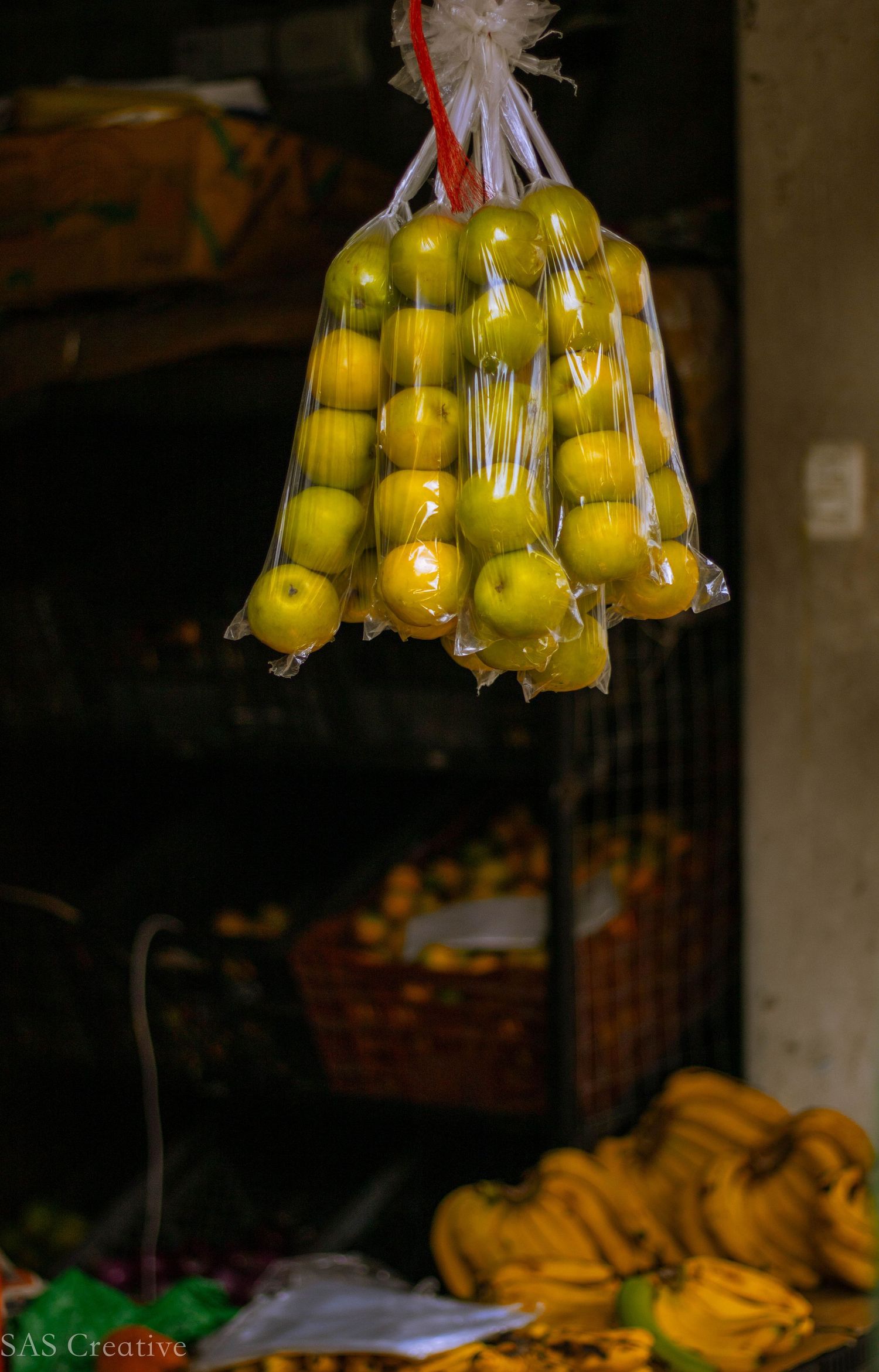 Fresh yellow-green apples bundled in clear plastic bags hanging at an outdoor market stall.