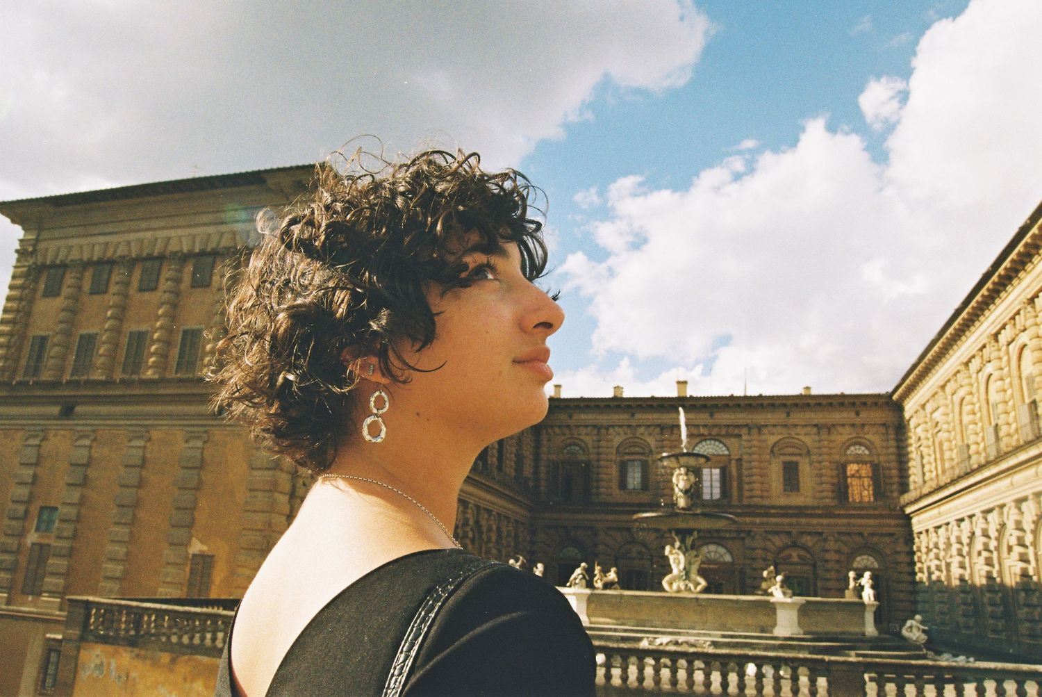 Young woman with curly hair poses in front of Palazzo Pitti fountain in Florence, Italy on a cloudy day.