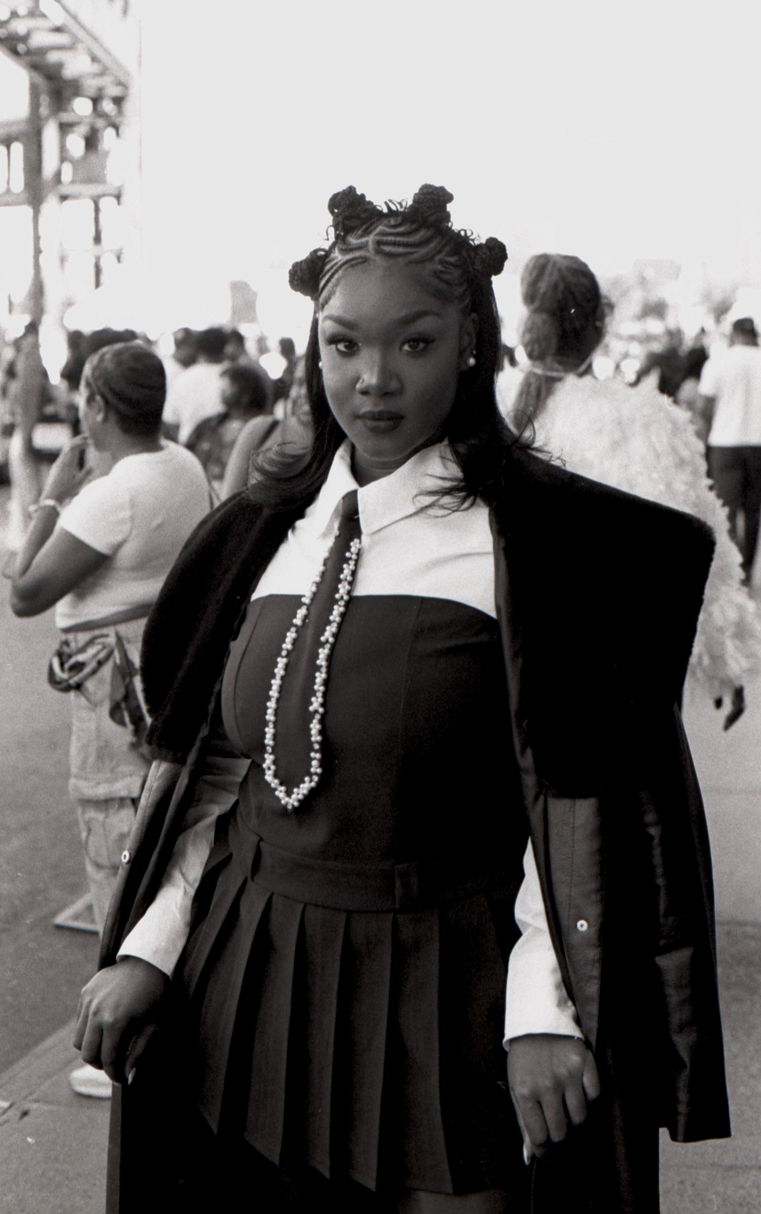 Black and white portrait of a young woman in a black outfit with braided hair at an outdoor event.