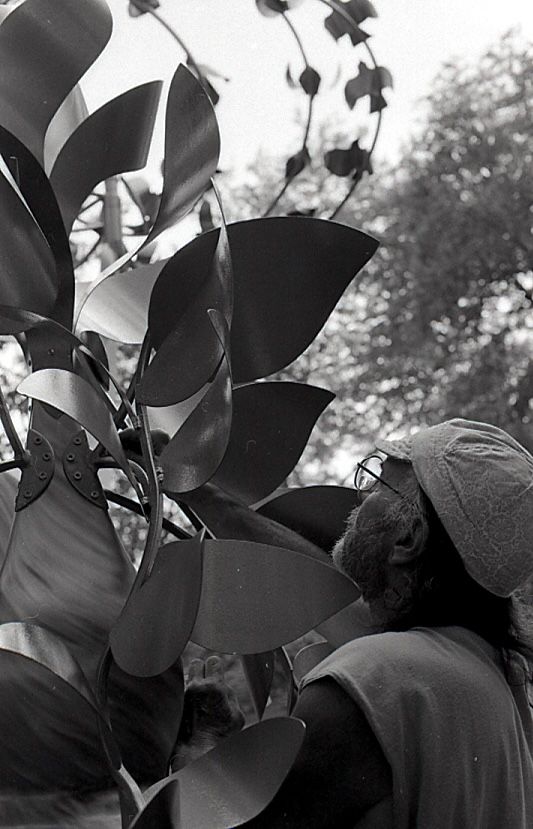 Black and white close-up of an artist inspecting intricate metal leaf details on a sculpture.