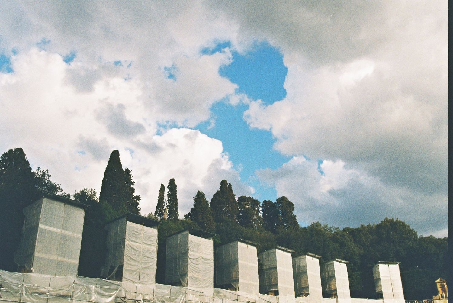 Row of white marble columns with cypress trees and dramatic cloudy sky in Florence, Italy.