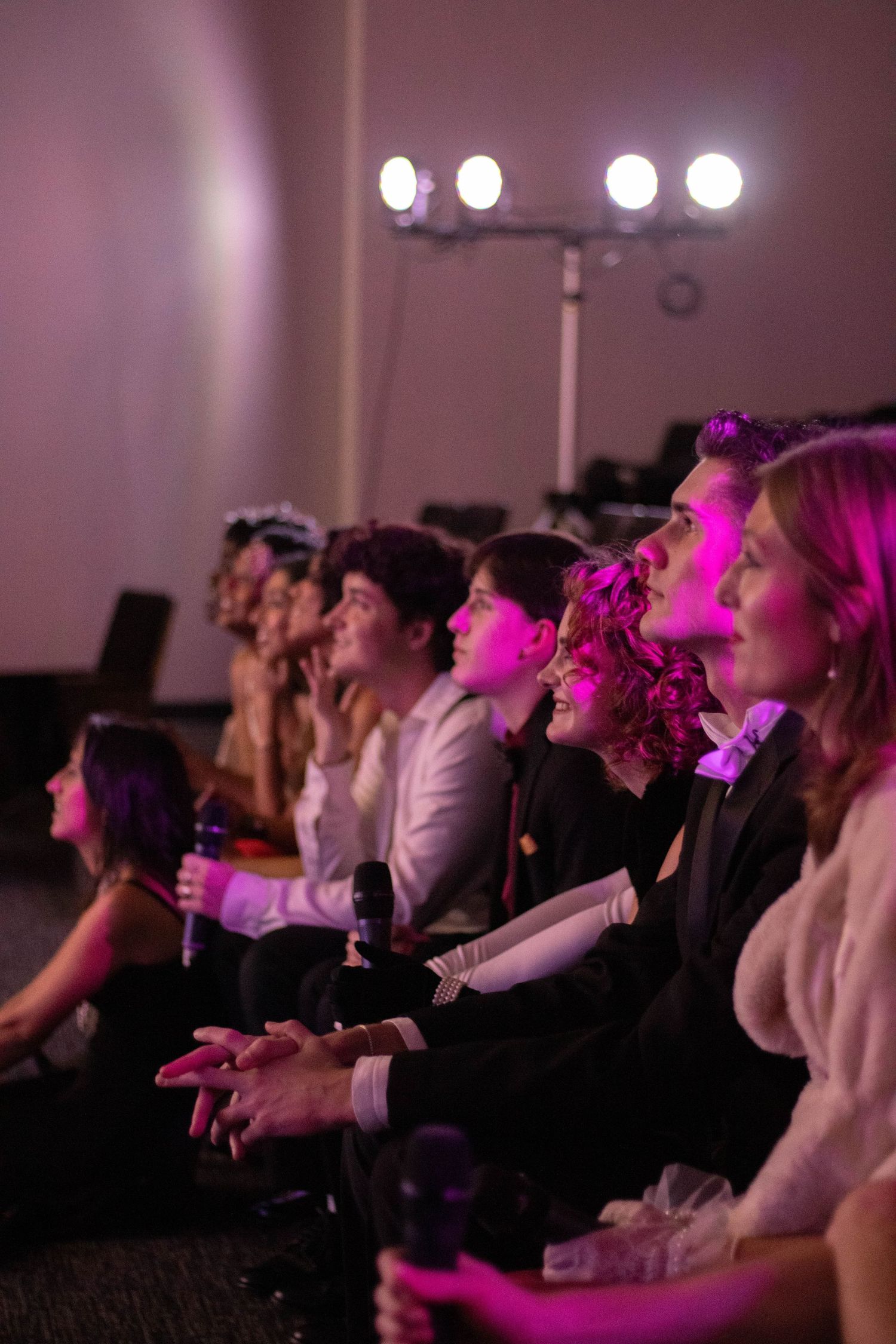 Group of young people sitting together at an event under pink stage lighting.