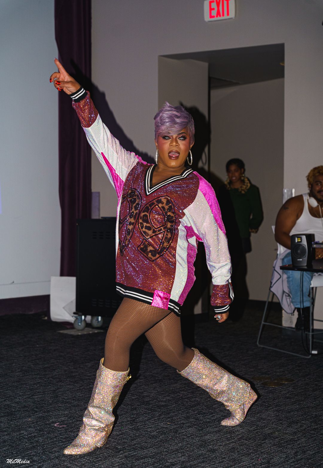 Performer in pink sequin cheerleader outfit and glitter boots strikes dynamic pose indoors.