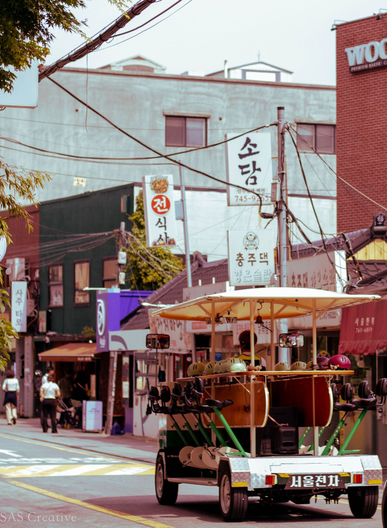 A colorful electric tourist vehicle on a busy Korean street lined with signs and traditional buildings.