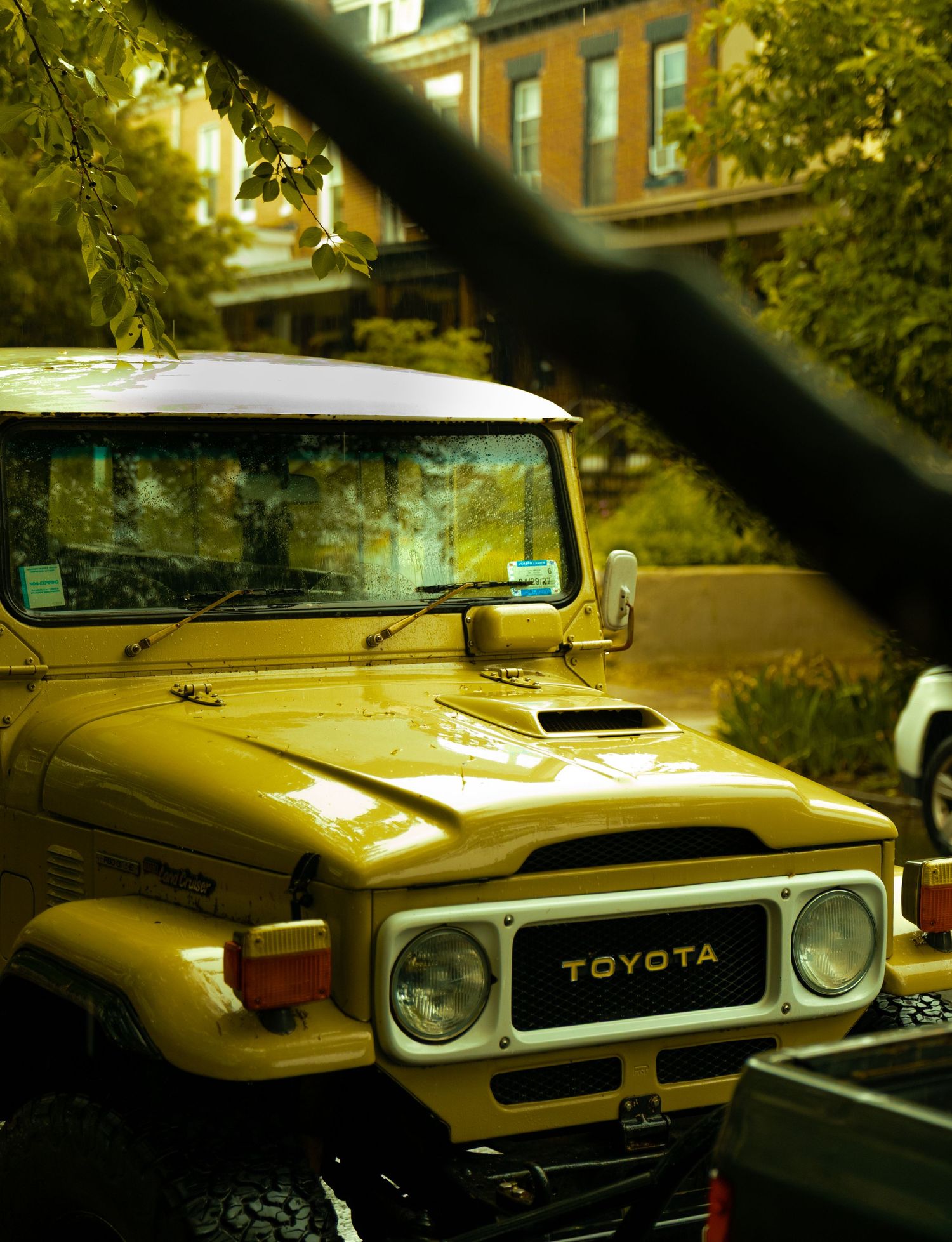 Vintage yellow Toyota FJ40 Land Cruiser parked on a tree-lined urban street on an autumn day.