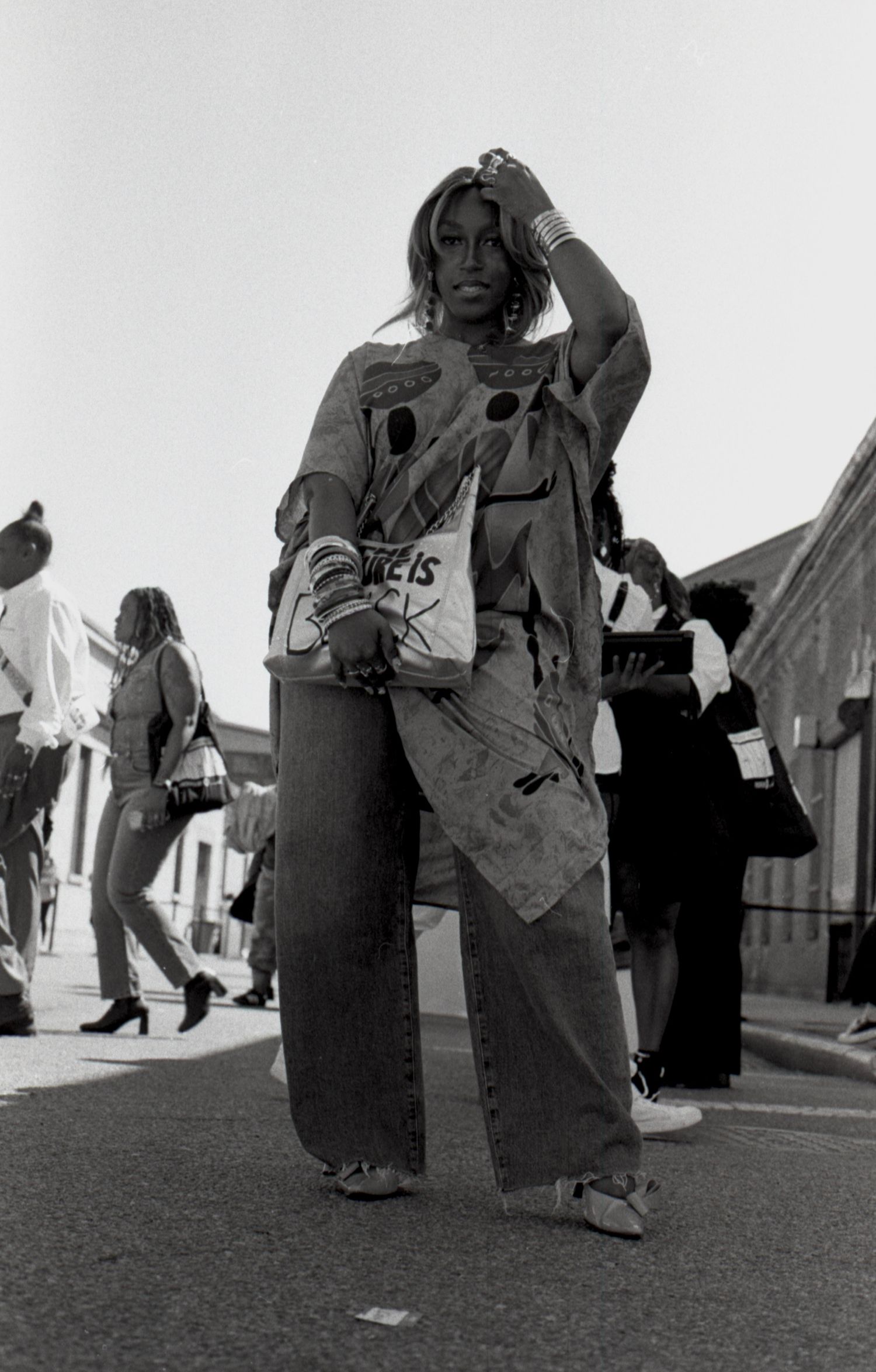 Black and white street photo of a stylish woman in oversized jeans and graphic sweatshirt on a busy street.