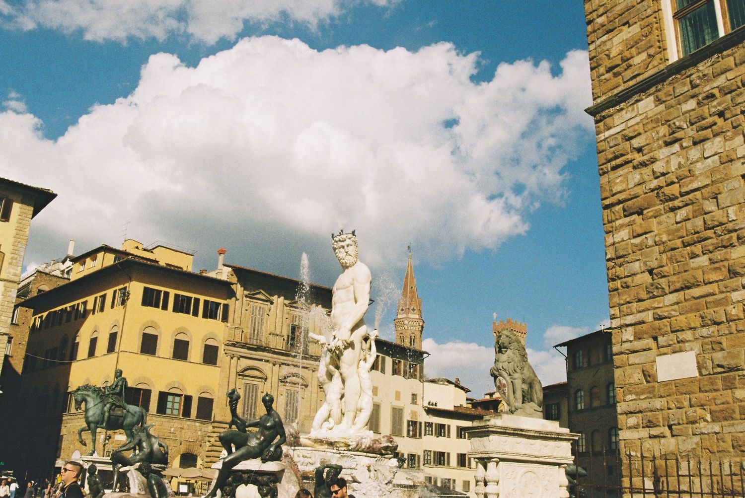 The Fountain of Neptune statue stands prominently in Piazza della Signoria, Florence, under a partly cloudy sky.
