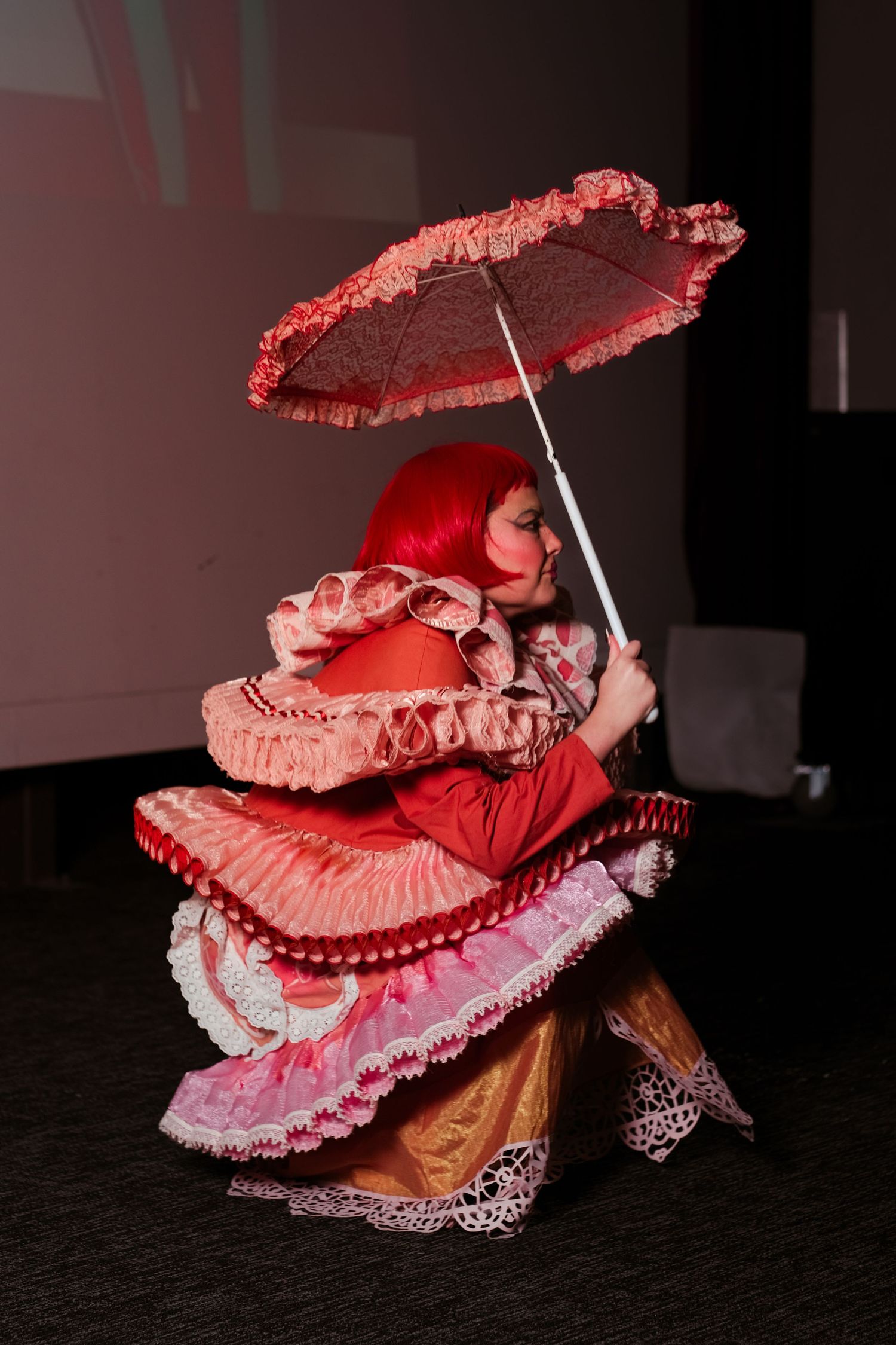 Performer in red ruffled dress with red hair twirling a decorative pink parasol umbrella.