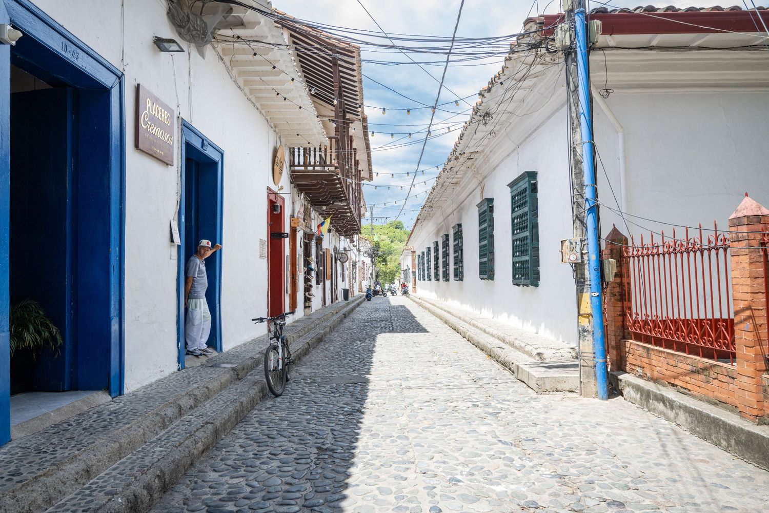 Narrow cobblestone street with white walls and blue trim details in a colonial Latin American town.