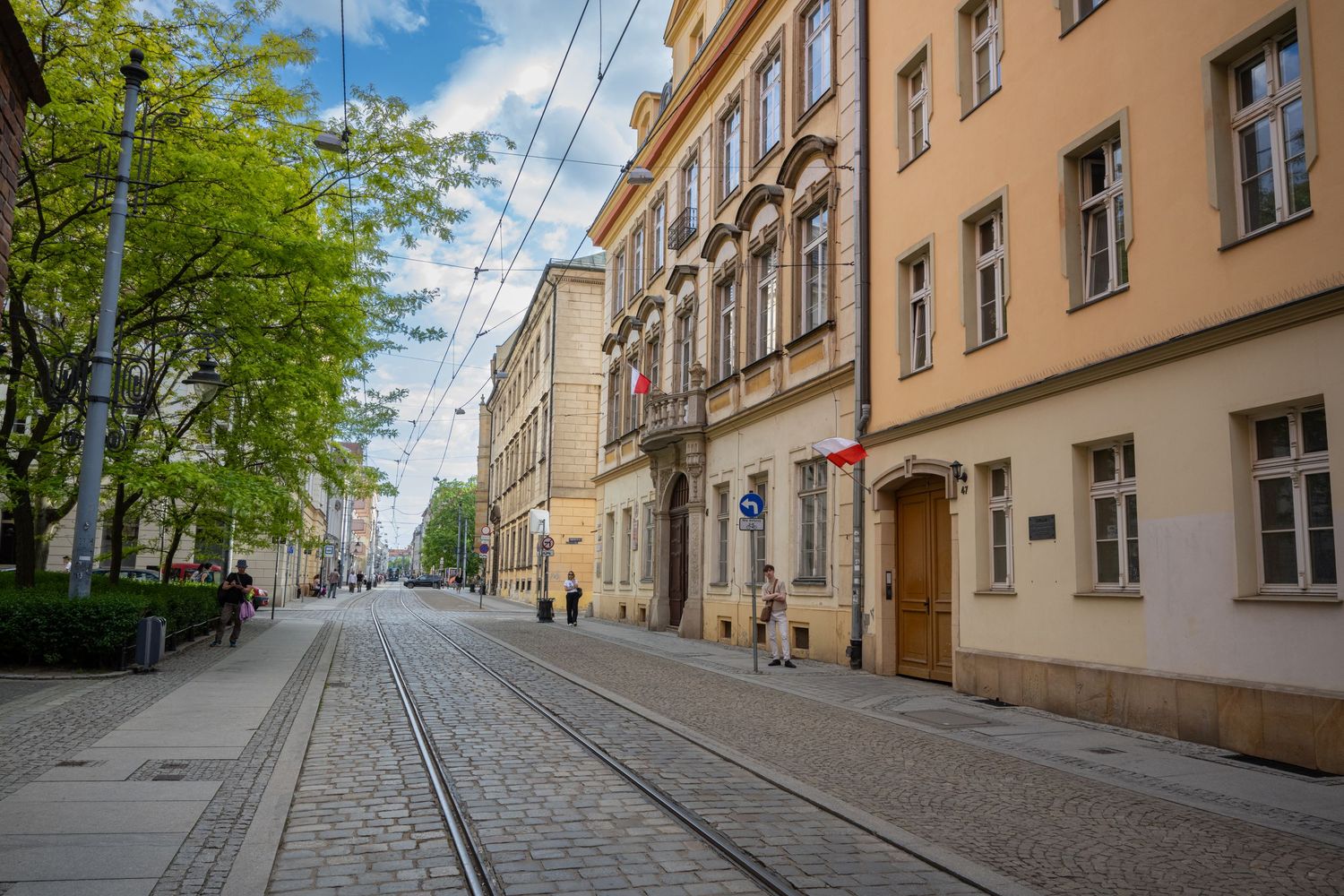 A quiet cobblestone street lined with historic beige buildings and tram tracks in an old European city district.