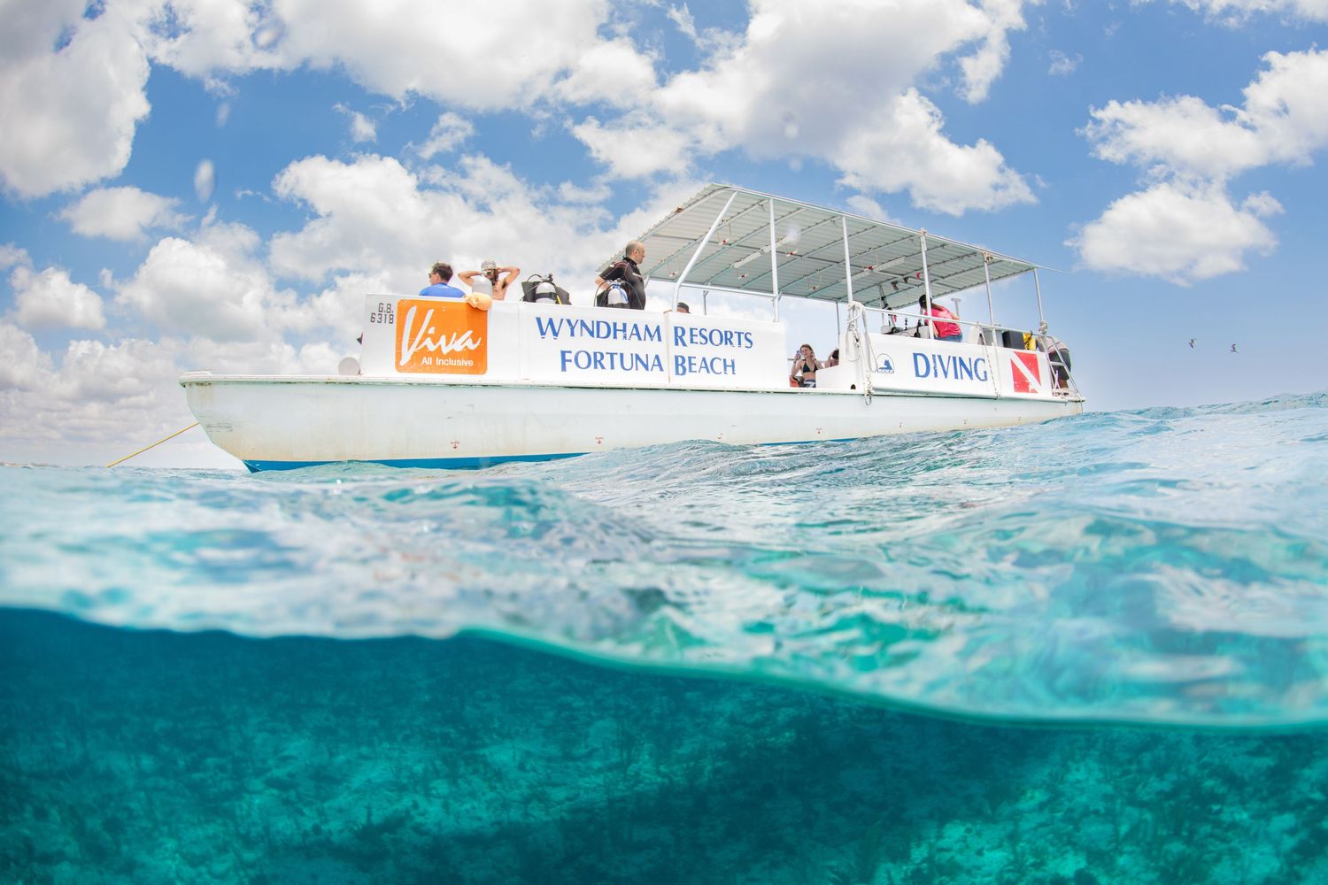 A split-view photograph shows a boat on turquoise waters with half the frame underwater revealing clear Caribbean waters.
