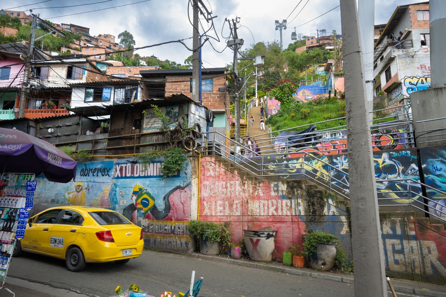 Colorful street art and graffiti adorns the hillside favela walls while a yellow taxi drives through Medellin, Colombia.