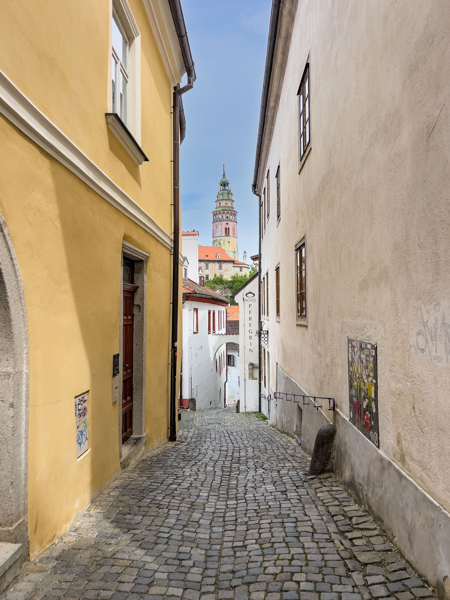 Narrow cobblestone alley winding between historic yellow and white buildings in a medieval European town.